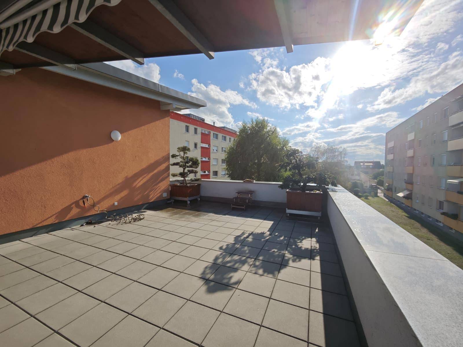 Sonnige Dachterrasse mit Fliesenboden und weitem Blick über die Umgebung.