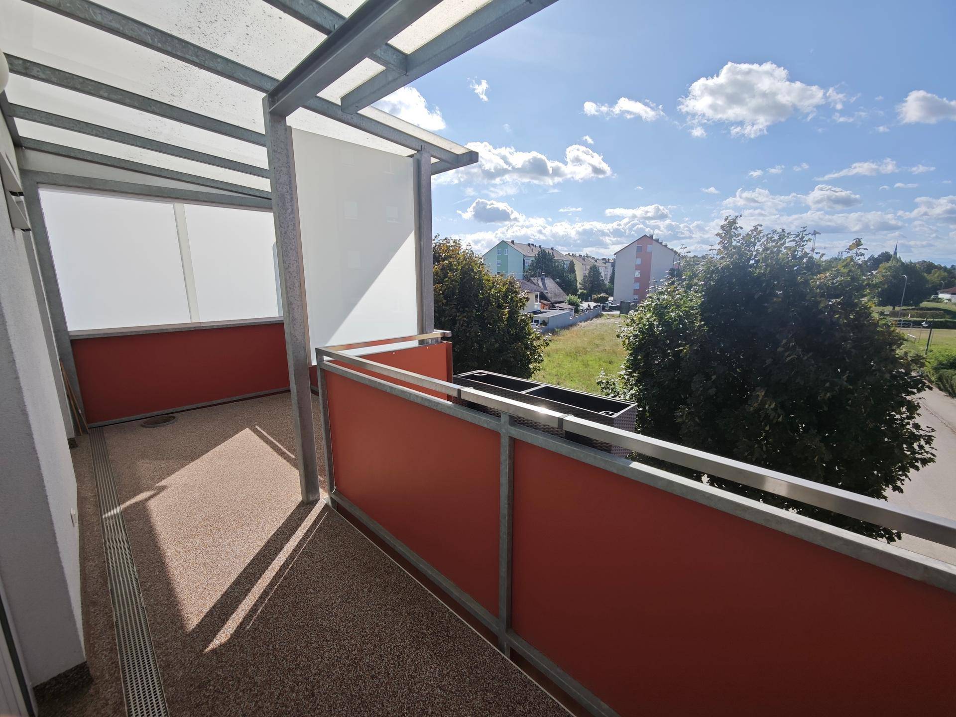 Heller Balkon mit orangefarbenem Geländer und Blick ins Grüne.
