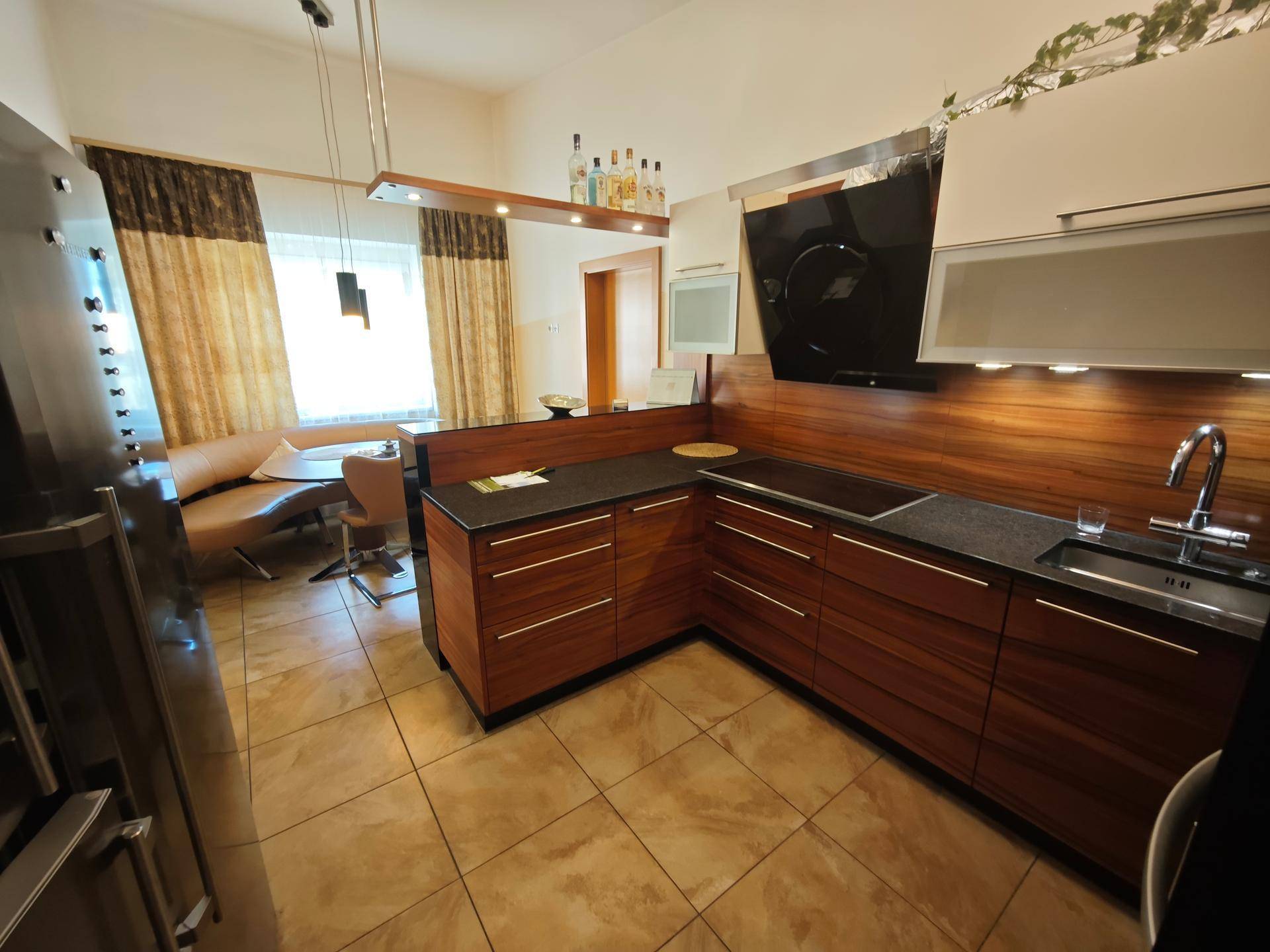 Moderne Küche mit Holzelementen, dunkler Arbeitsplatte und Essbereich im Hintergrund.