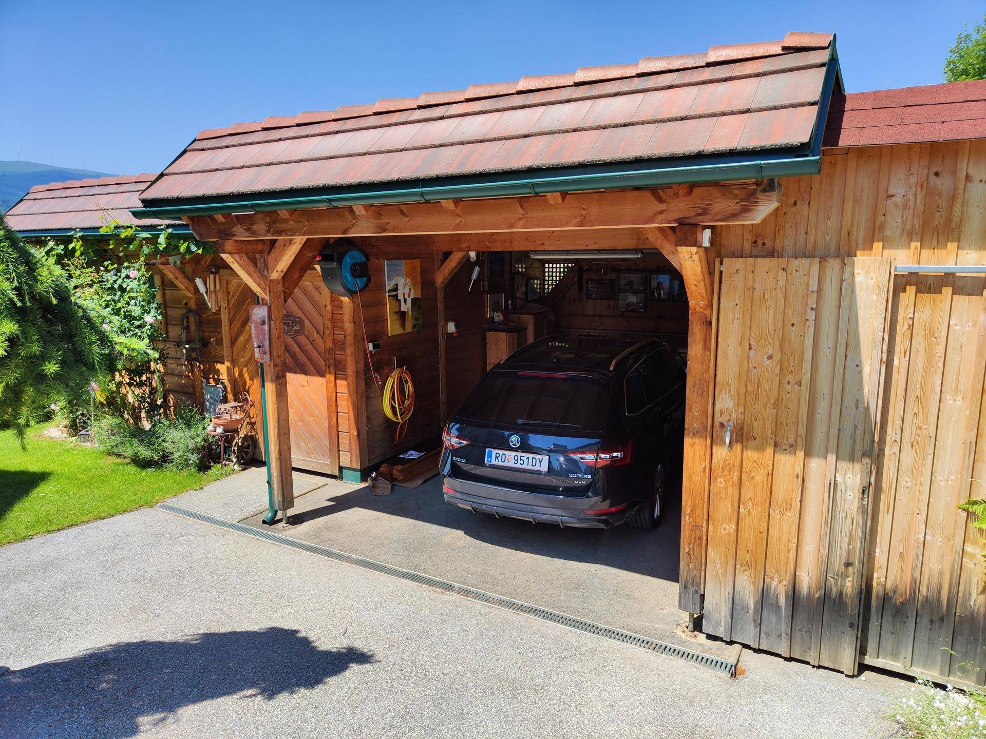 Überdachter Garagenbereich aus Holz mit Platz für ein Fahrzeug und Stauraum für Gartengeräte.