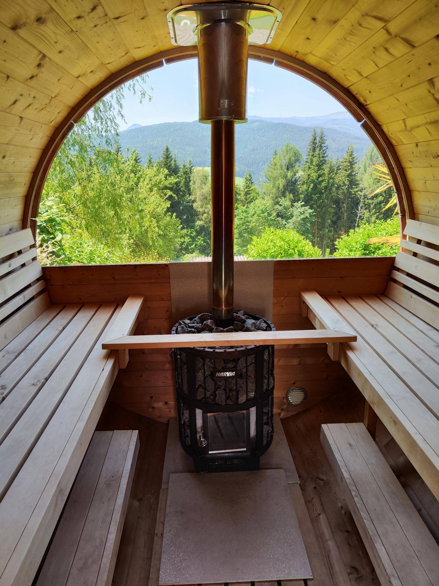 Fasssauna aus Holz mit Blick auf die Berge, ausgestattet mit einem traditionellen Saunaofen.
