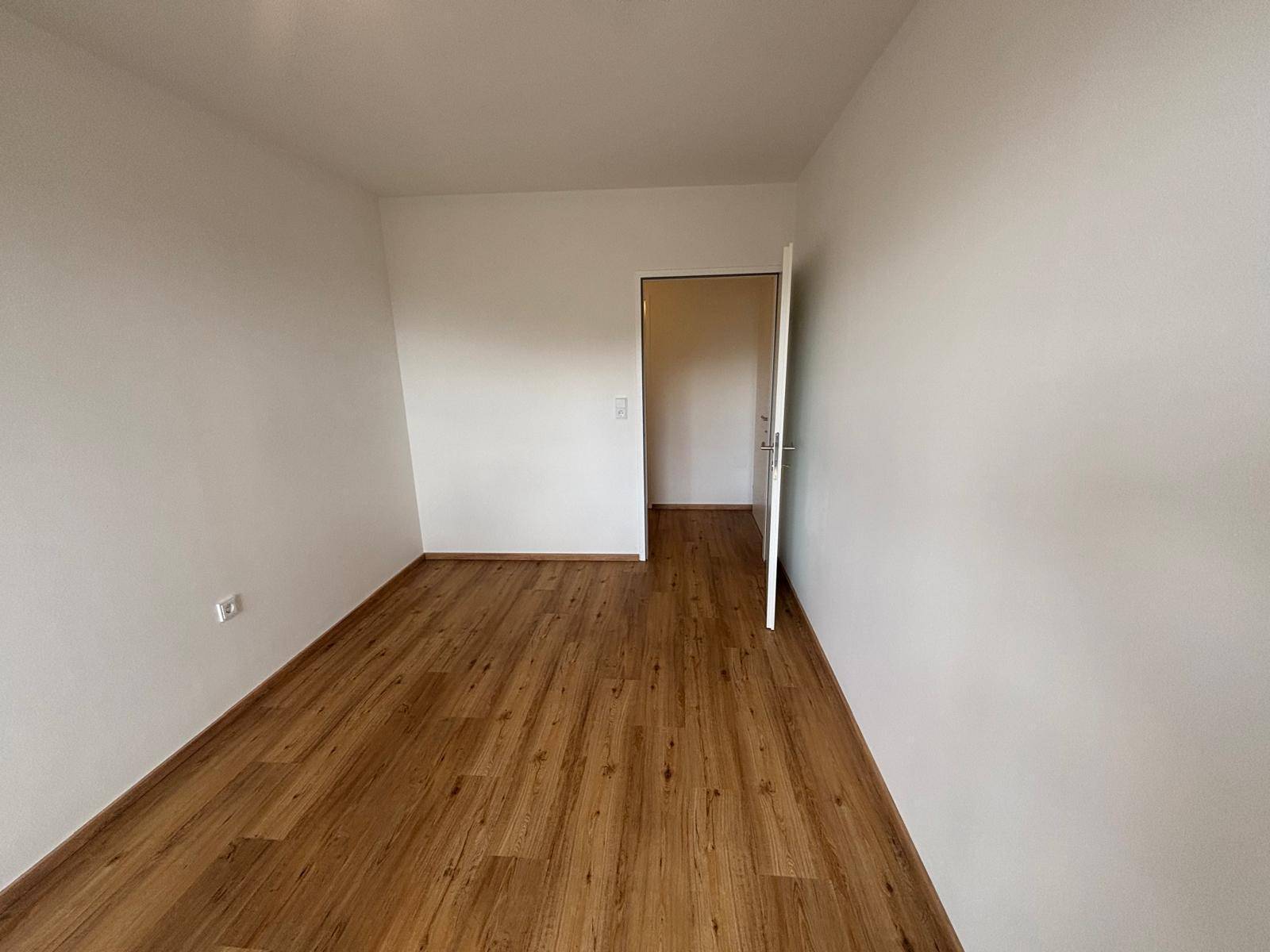 Schmaler Flur mit Laminatboden und weißen Wänden, der zu einem weiteren Raum führt.