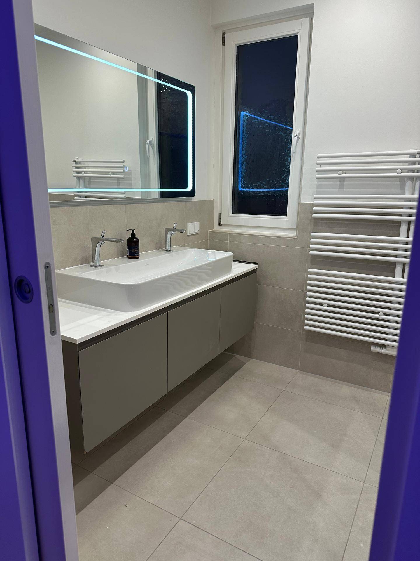 Modernes Badezimmer mit Waschtisch, beleuchtetem Spiegel und Handtuchheizkörper.