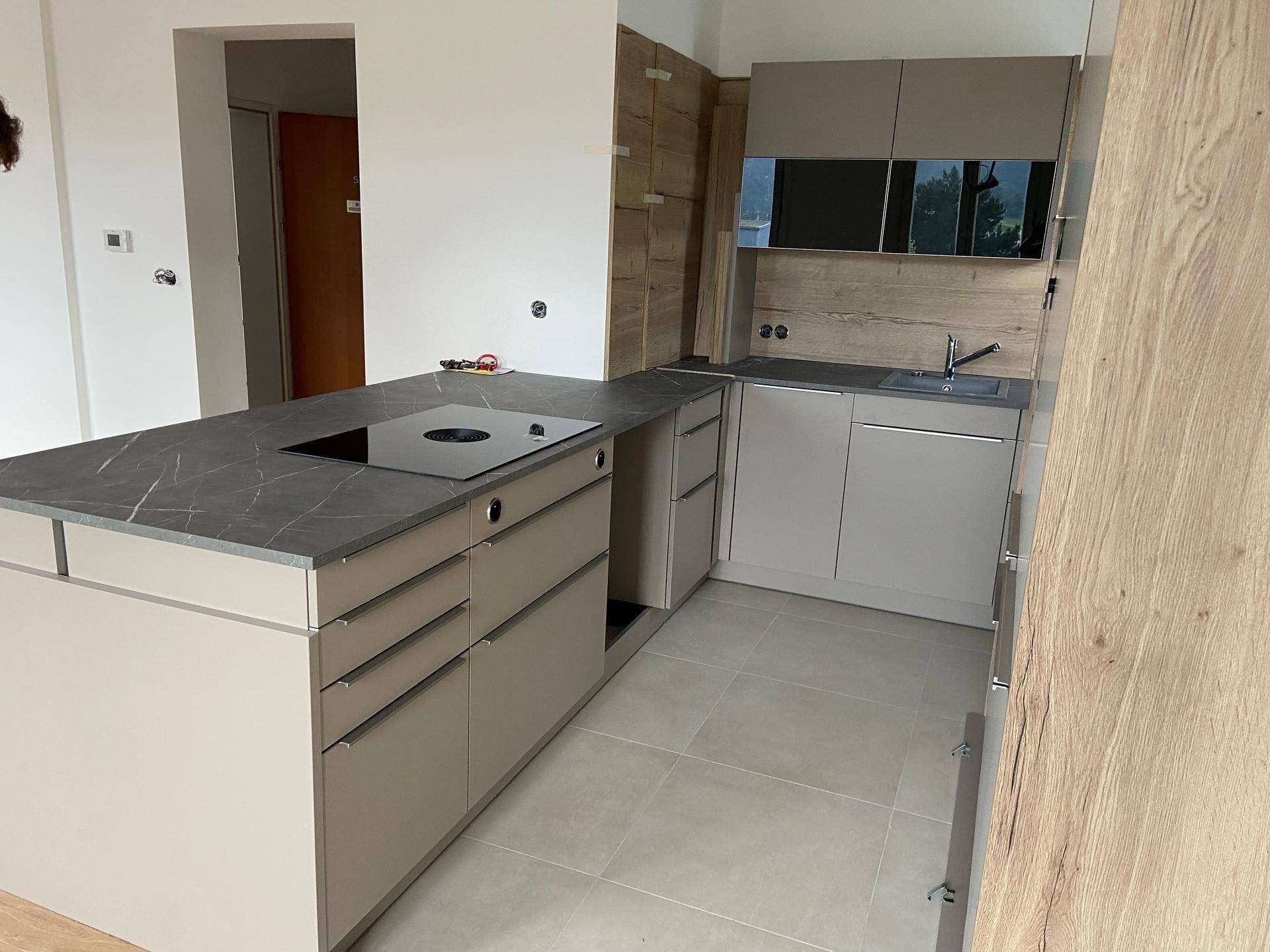 Moderne Einbauküche mit grauen Schränken, dunkler Arbeitsplatte und Induktionskochfeld.