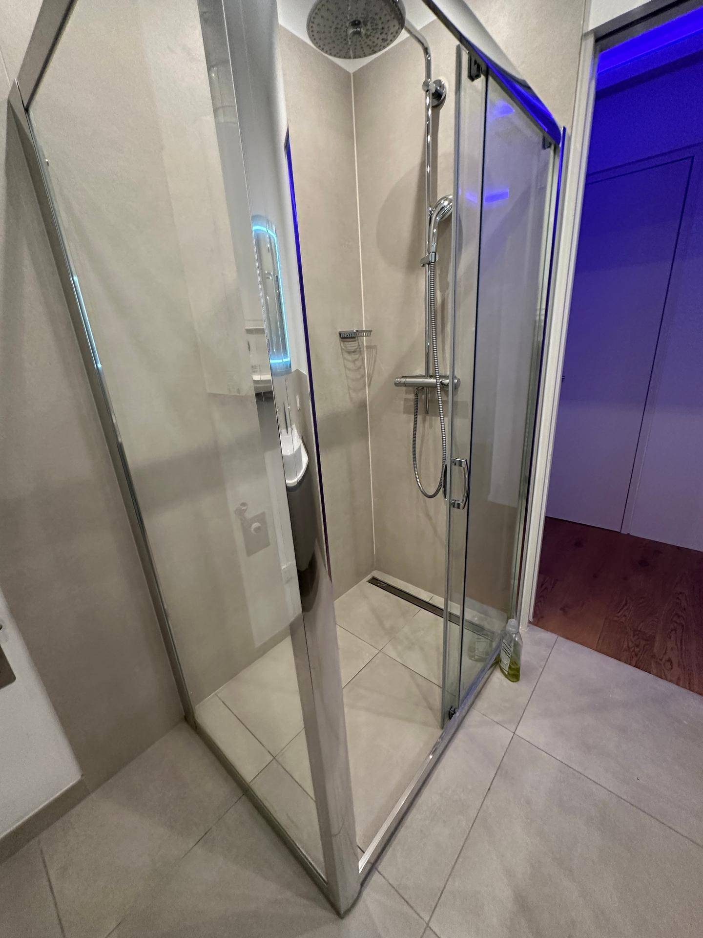 Moderne Duschkabine mit Glaswänden und Regenduschkopf in hellem Badezimmer.