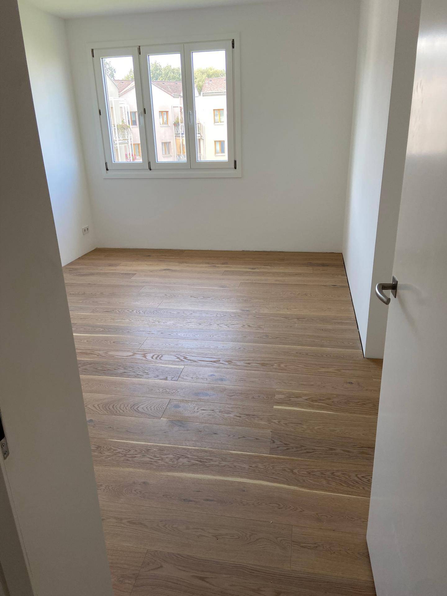 Leeres Schlafzimmer mit neuem Echtholz-Dielenboden und Blick nach draußen.