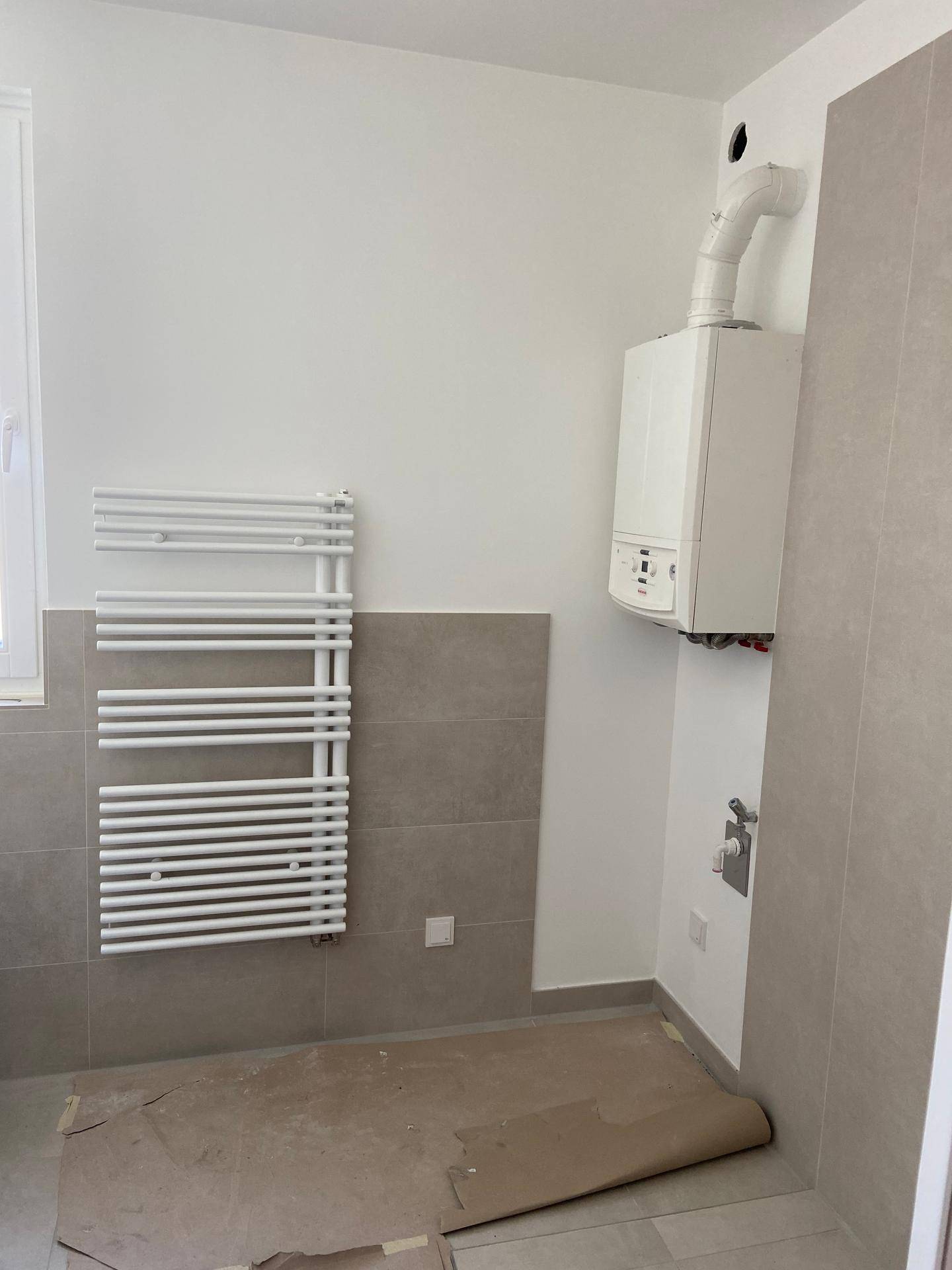Badezimmer im Rohbau mit Heiztherme und modernem Handtuchheizkörper.
