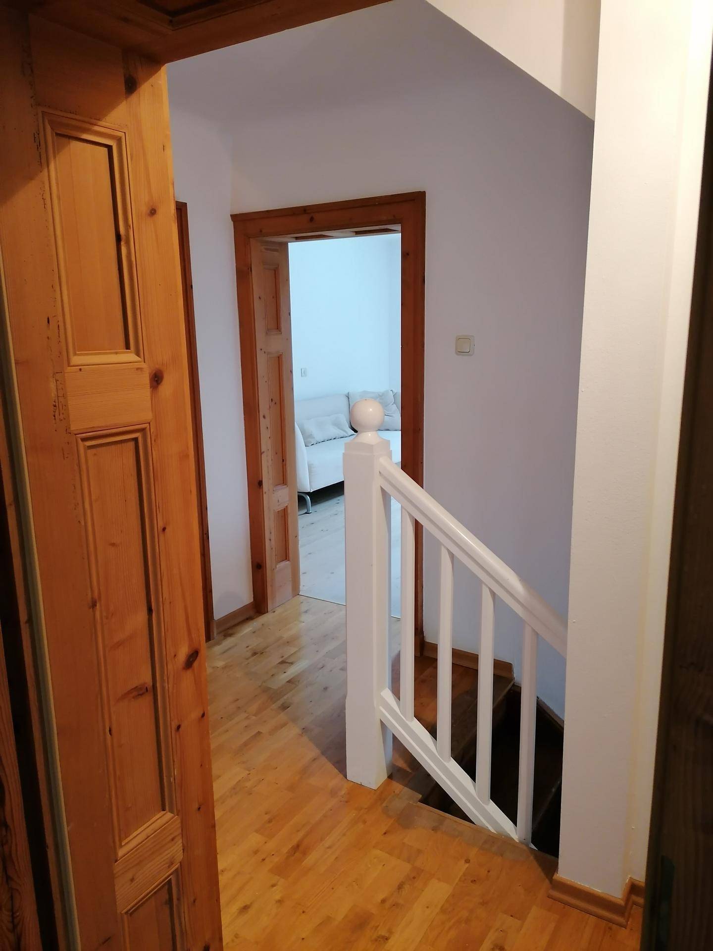 Heller Flur mit Holzparkett und einer weißen Treppe, die in die obere Etage führt.