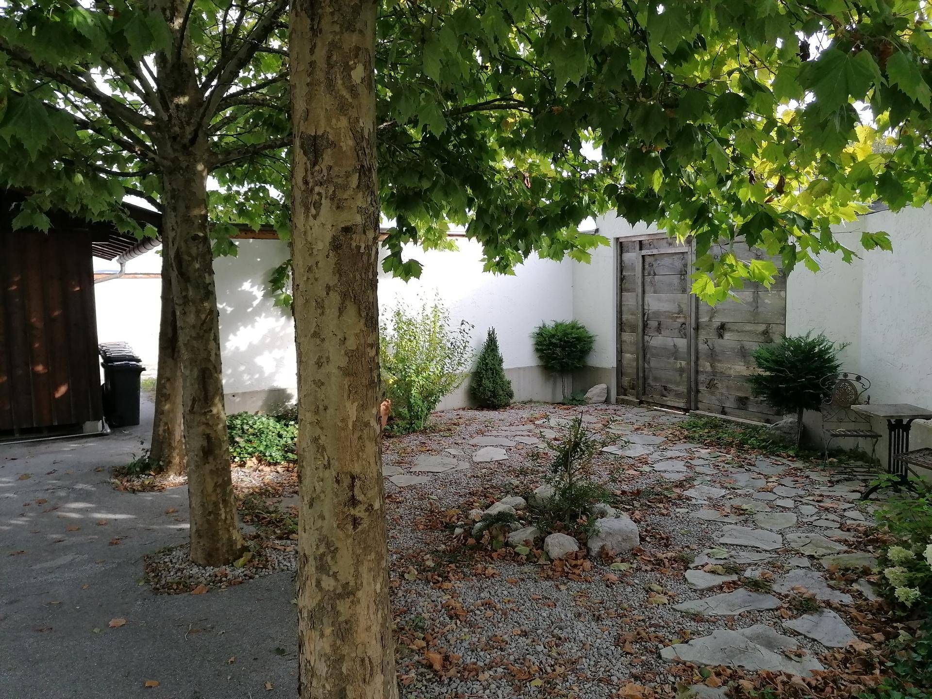 Ruhiger Innenhof mit Bäumen, Steinplatten und einer kleinen Sitzecke im Freien.