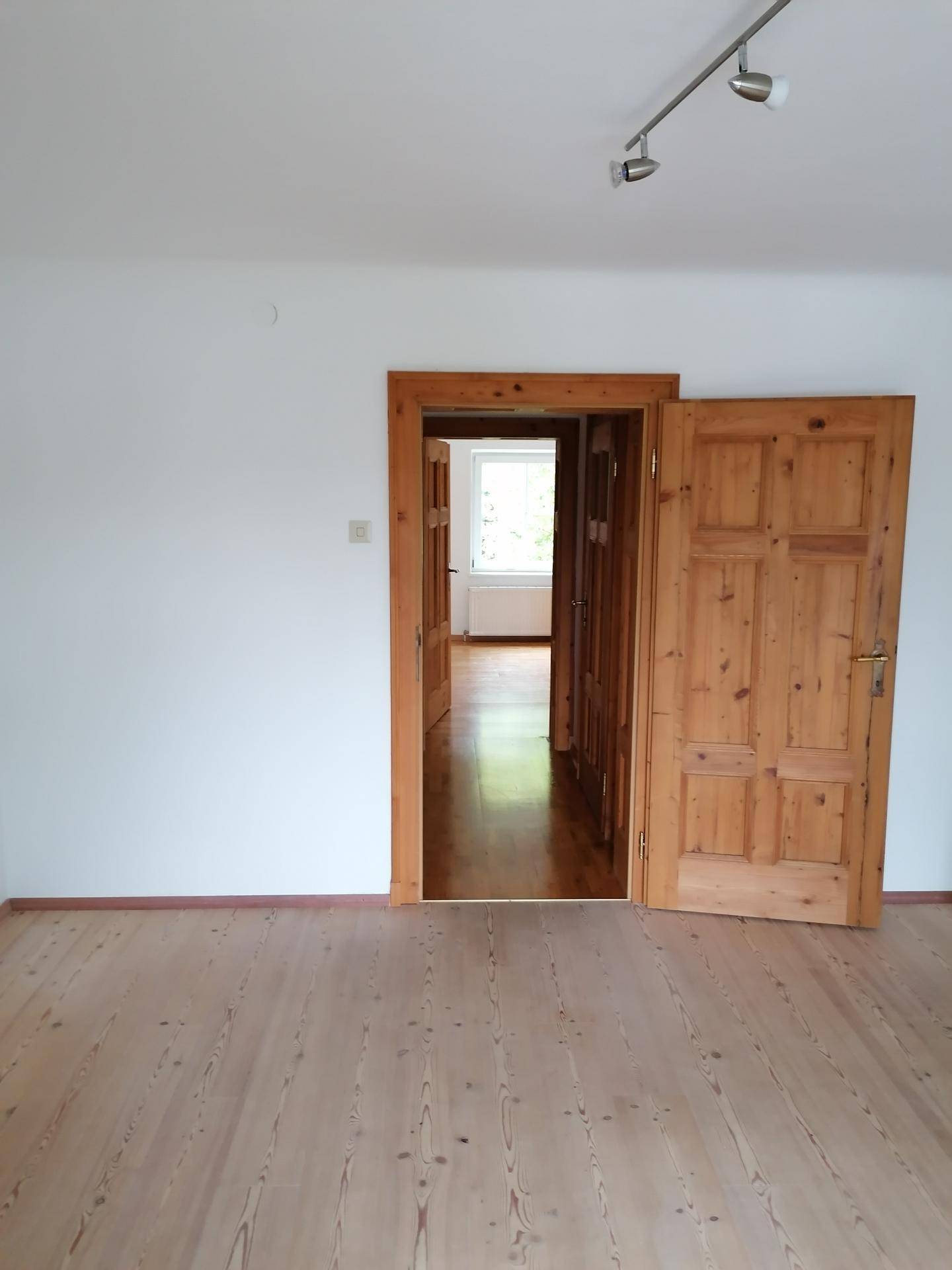 Leerer Raum mit Holzboden und traditionellen Holztüren, die zu weiteren Zimmern führen.