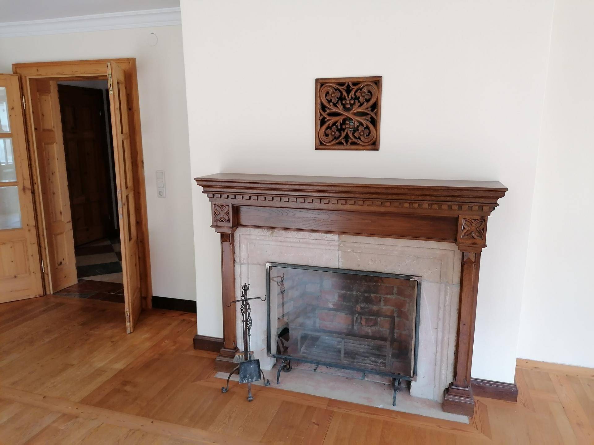 Helles Wohnzimmer mit Holzboden und einem klassischen Kamin mit Holzmantel als Blickfang.