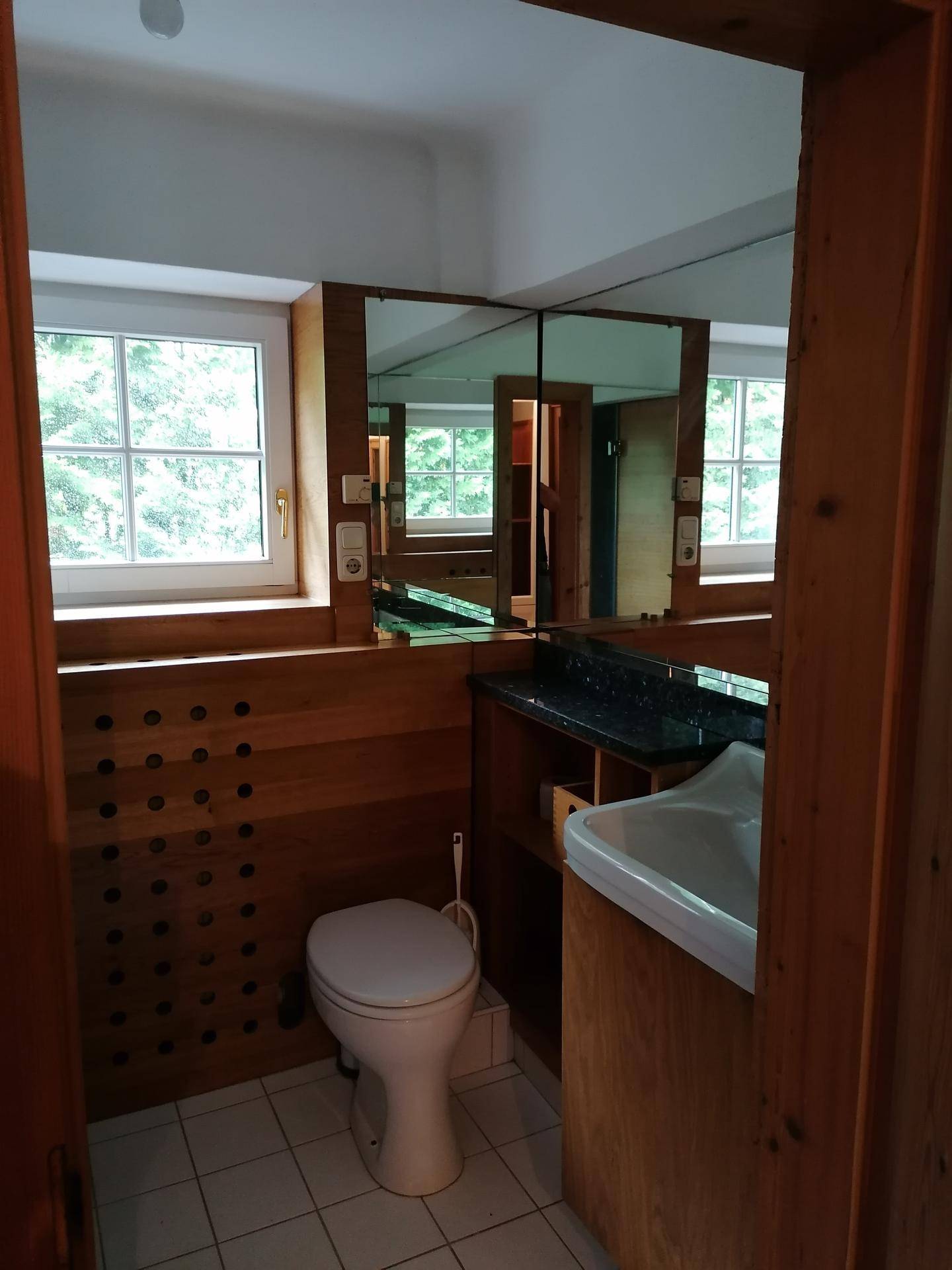 Kleines WC mit Fenster, Holzverkleidung und einem integrierten Spiegel über dem Waschbecken.