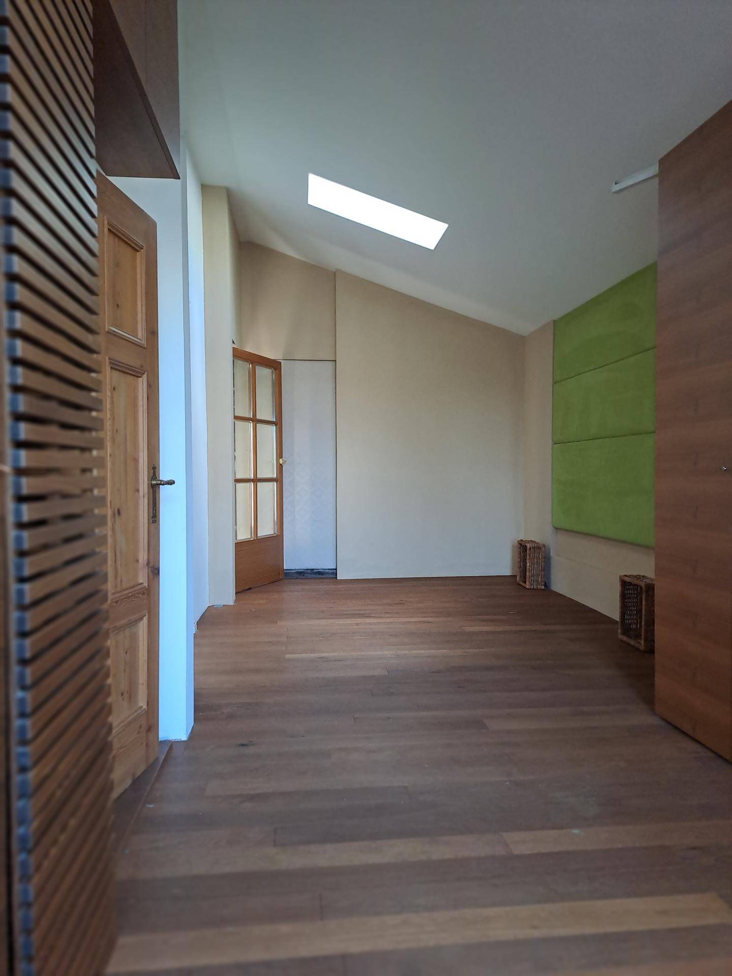 Heller Raum mit Dachschräge, Holzboden und einem Oberlicht für reichlich natürliches Licht.