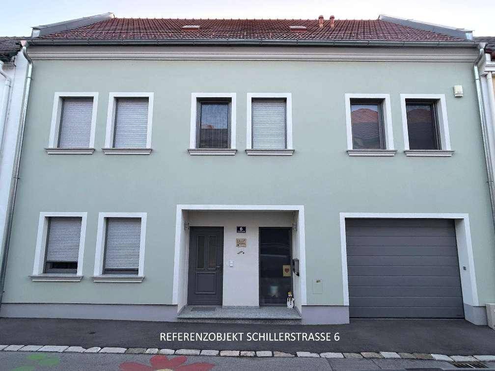 Fassade eines Wohnhauses mit hellgrüner Farbe, mehreren Fenstern und einem Garagentor.