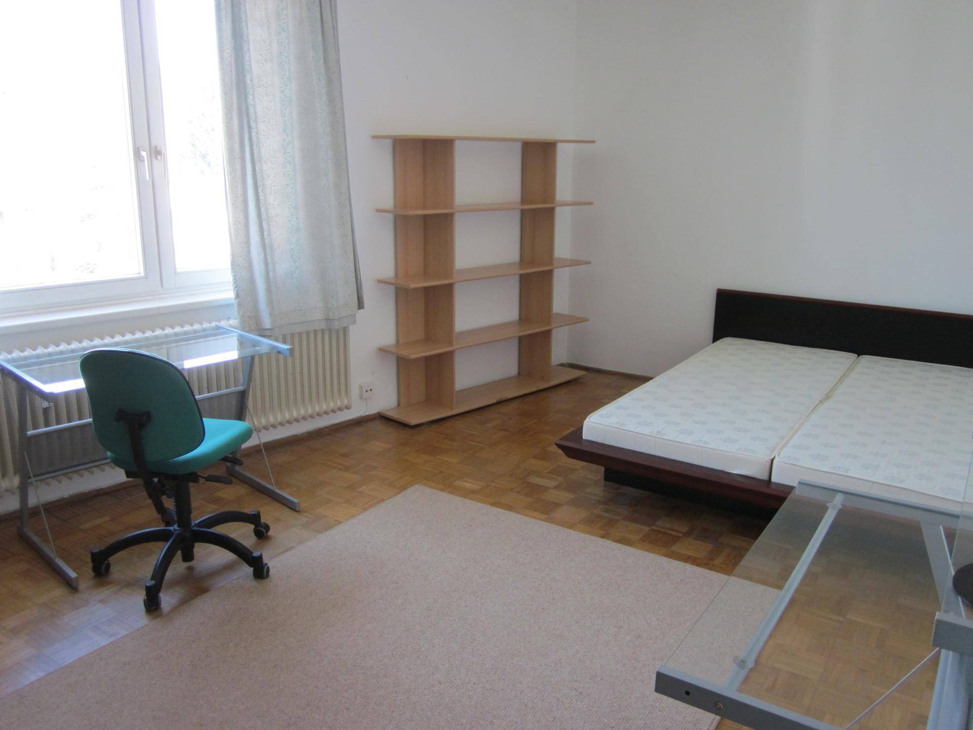 Helles Schlafzimmer mit Bett, Schreibtisch und Regal, bietet eine funktionale Einrichtung und viel Tageslicht.