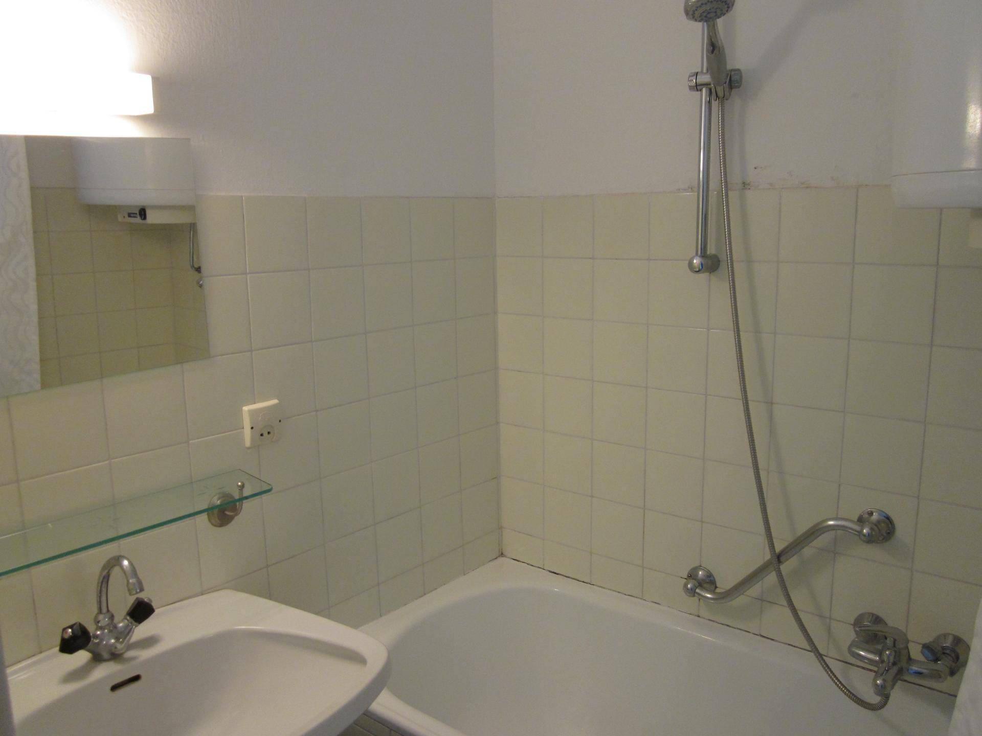 Funktionales Badezimmer mit Badewanne, Waschbecken und hellen Fliesen, ausgestattet mit grundlegenden Armaturen.