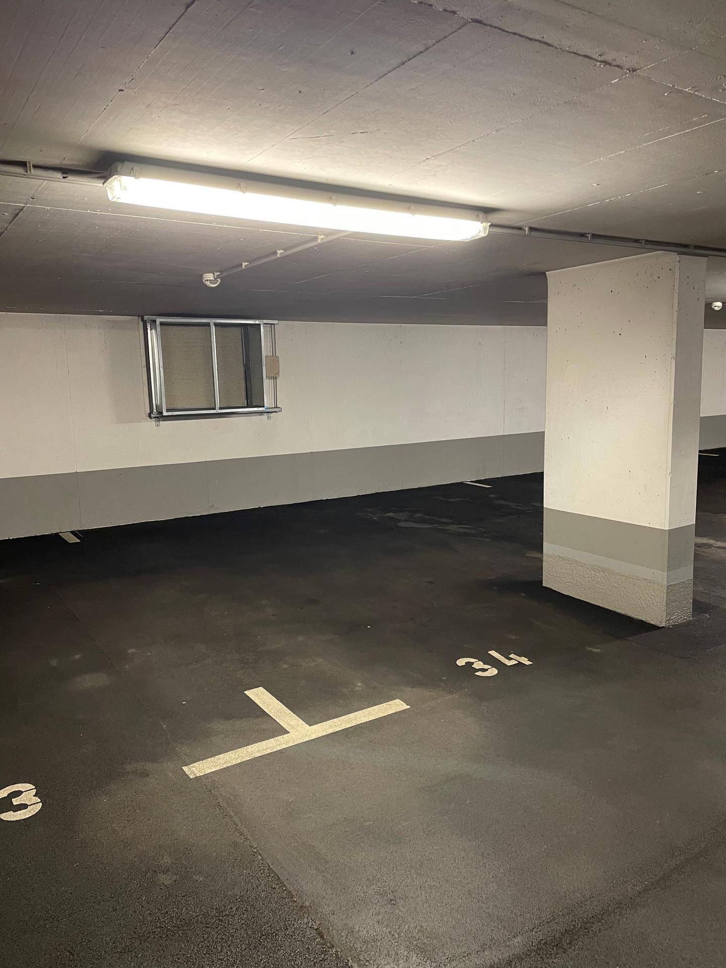 Geräumige Tiefgarage mit markierten Stellplätzen, einem kleinen Fenster und Beleuchtung.