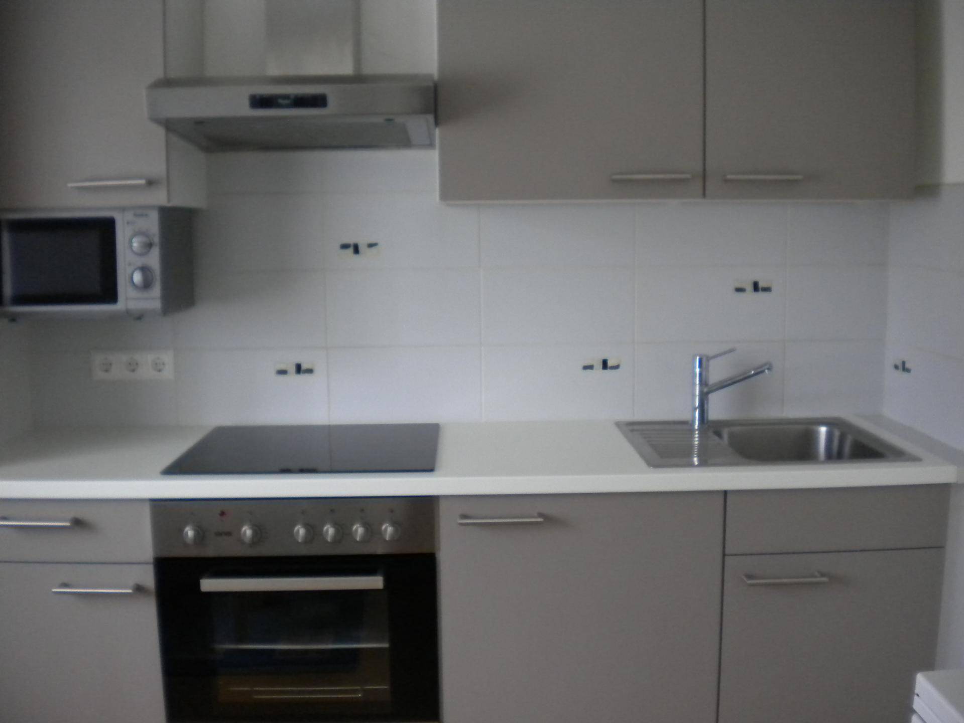 Moderne Küche mit grauen Schränken, Induktionskochfeld und integriertem Backofen.