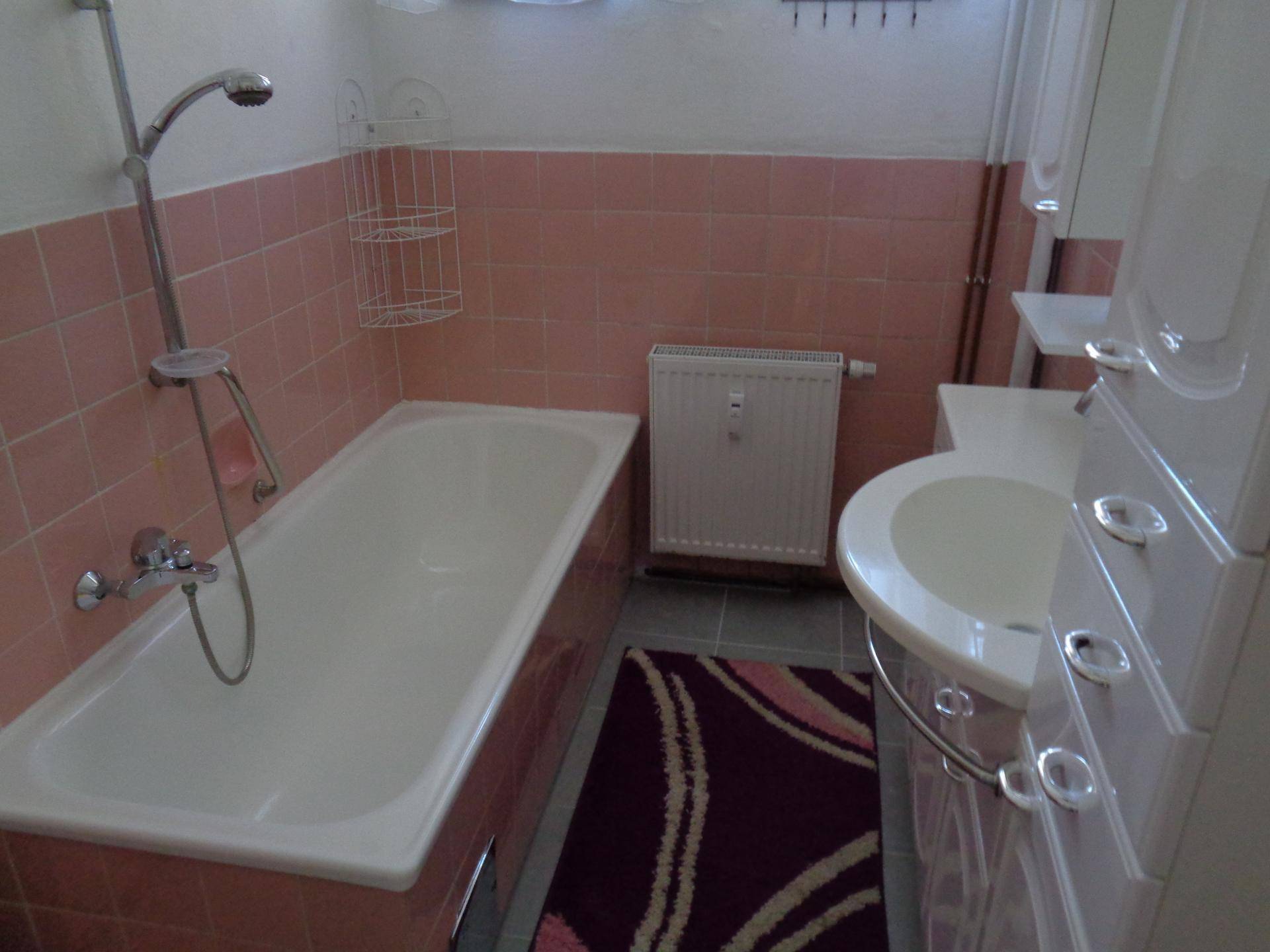 Badezimmer mit rosa Fliesen, Badewanne und Waschbecken mit Spiegelschrank.