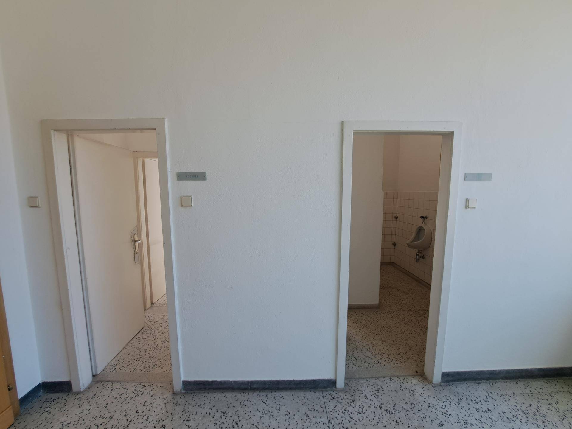 Flur mit zwei Türen, die zu Sanitärräumen führen, und Terrazzoboden.