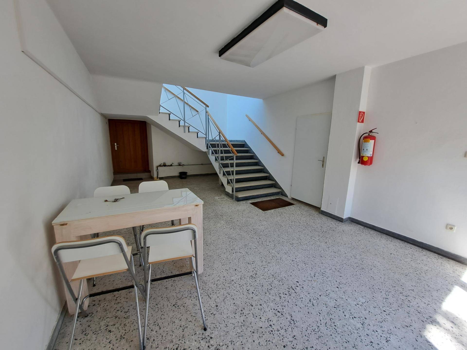 Geräumiger Flur mit Treppenaufgang, Tisch und Stühlen sowie Terrazzoboden.