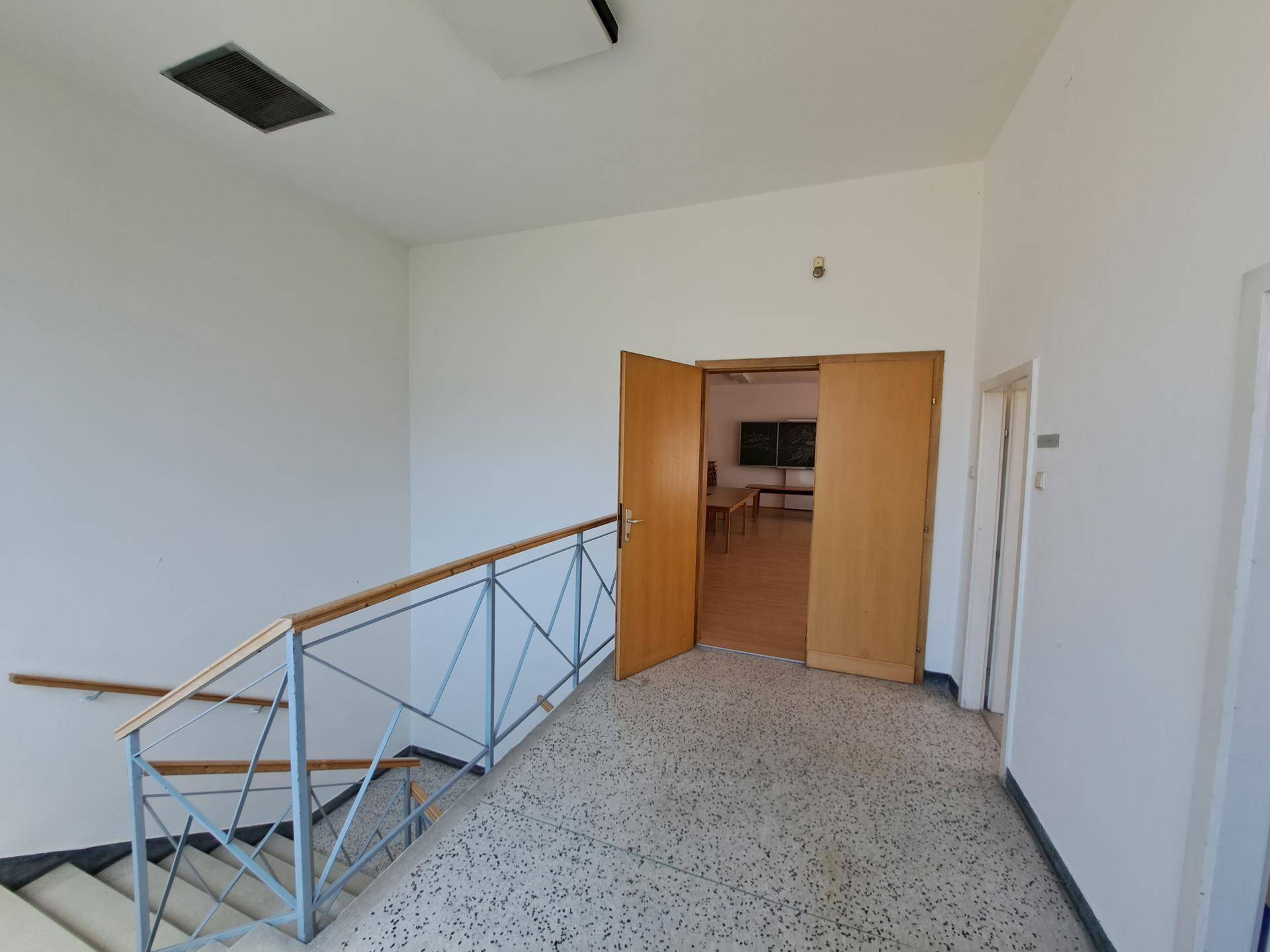 Treppenabsatz mit Terrazzoboden und Metallgeländer, eine Holztür führt in einen weiteren Raum.
