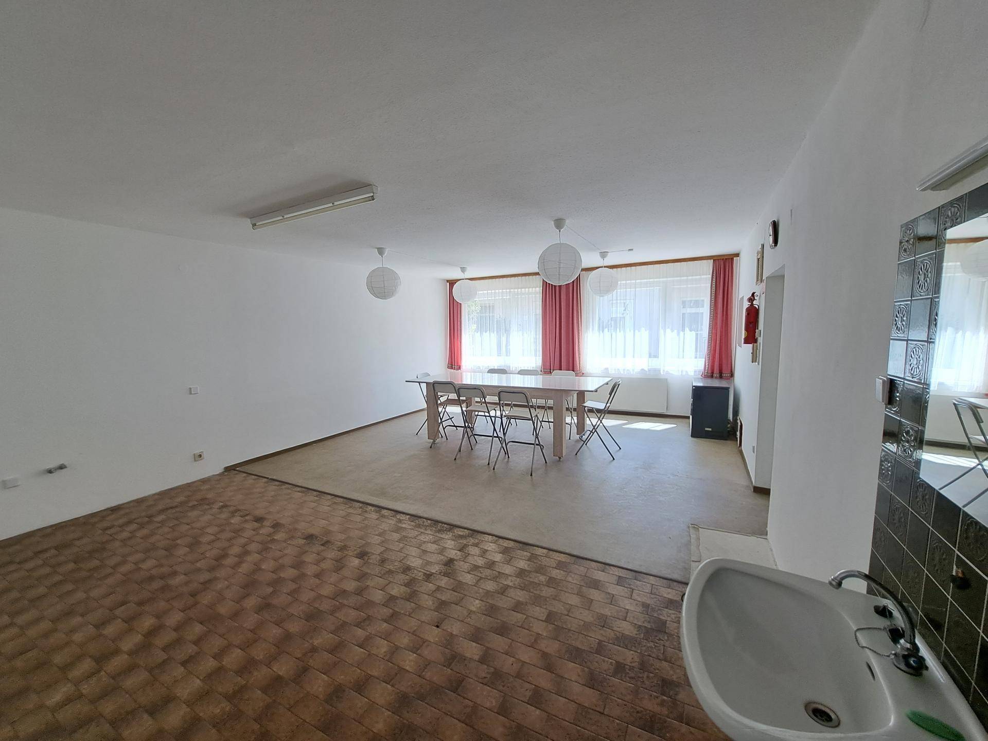 Großer Gemeinschaftsraum mit Esstisch, Fenstern und unterschiedlichen Bodenbelägen.