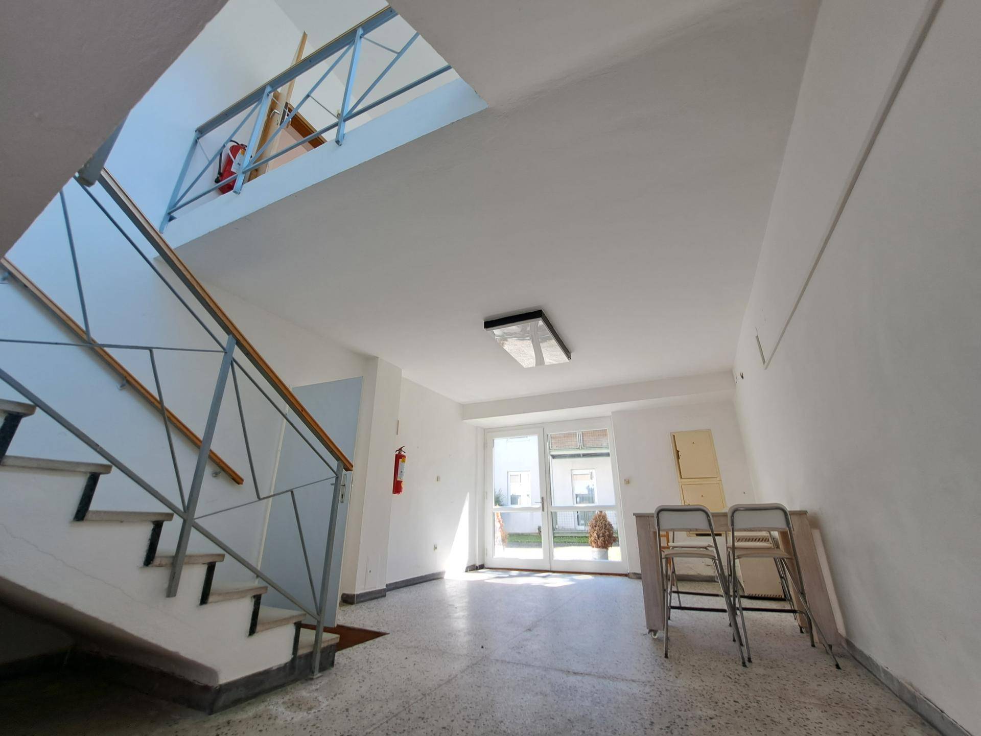 Geräumiger Flur mit Treppenaufgang und viel Tageslicht durch große Fenster.