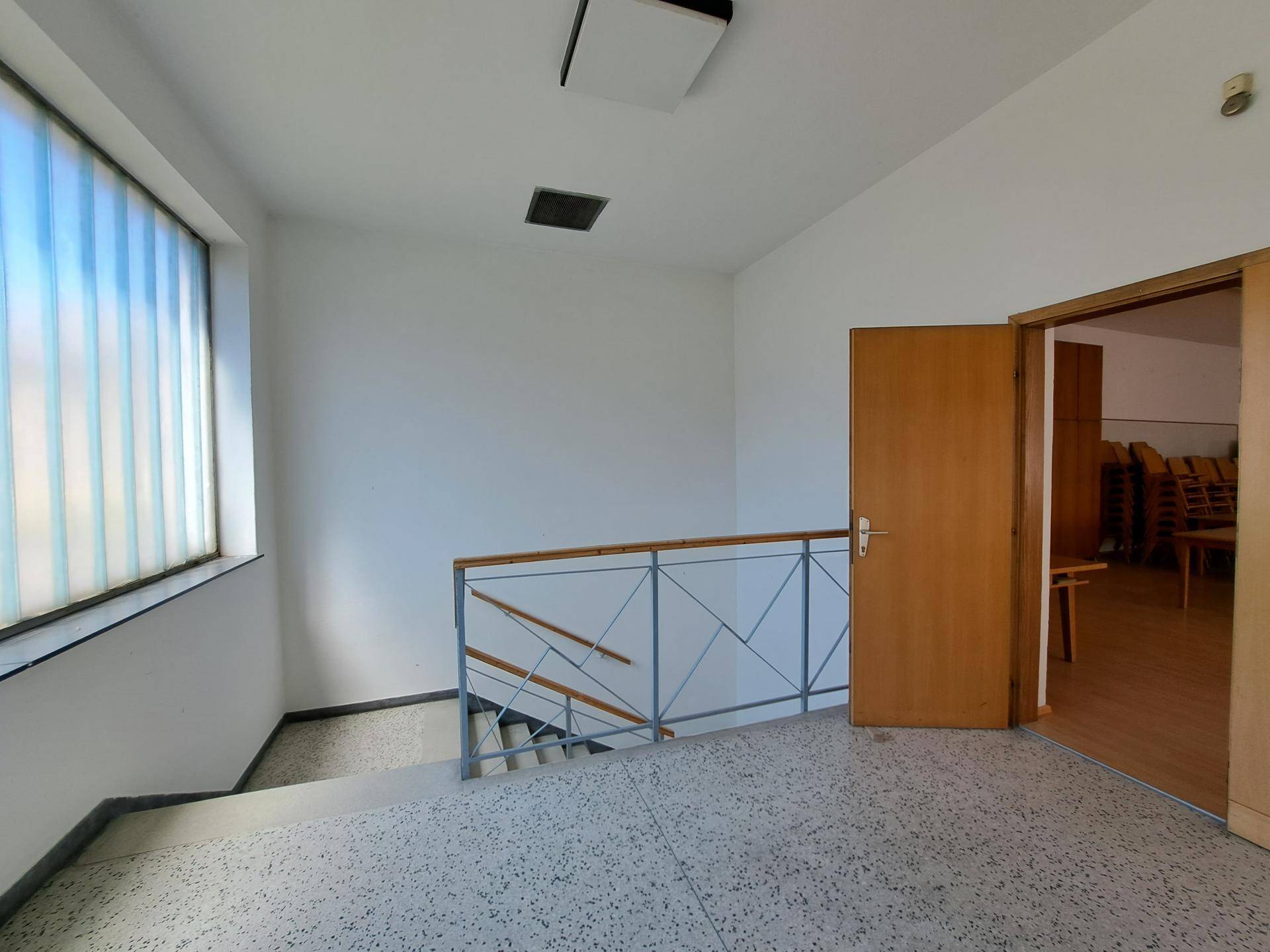 Treppenabsatz mit Terrazzoboden, Metallgeländer und einem großen Fenster aus Milchglas.