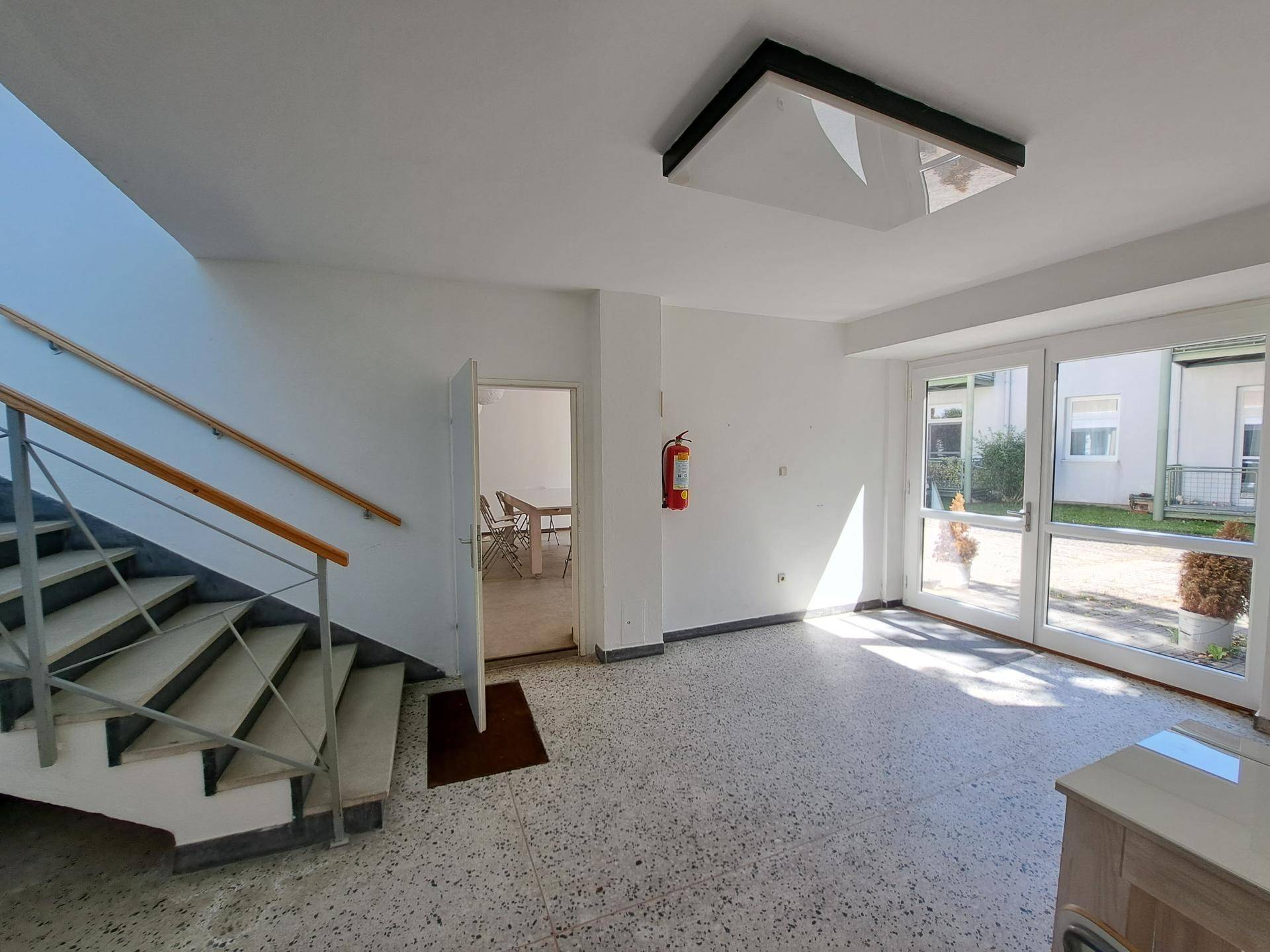 Heller Eingangsbereich mit Treppenaufgang und großen Glastüren zum Außenbereich.
