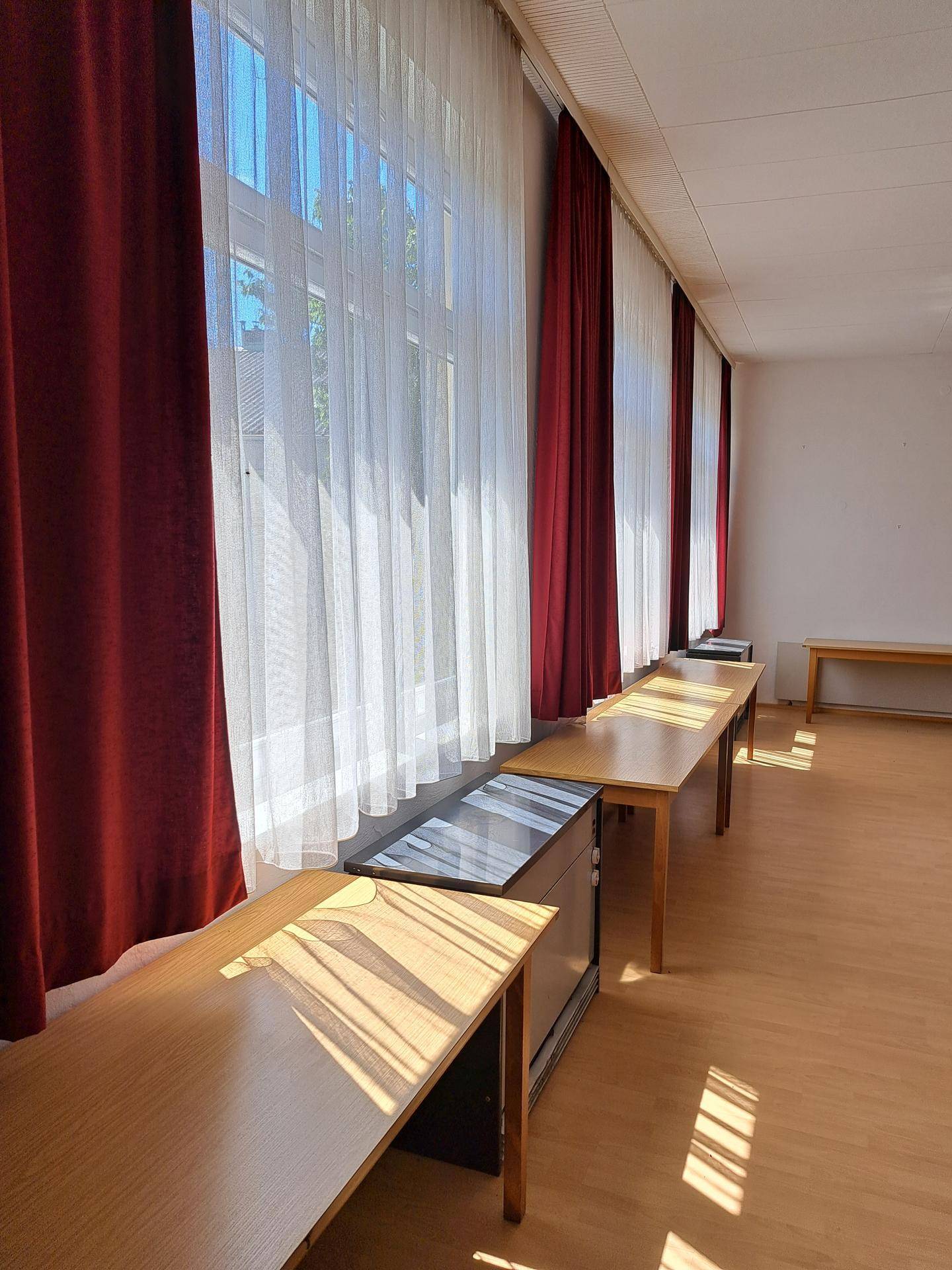 Große Fensterfront mit roten und weißen Vorhängen, die viel Sonnenlicht in den Raum lassen.