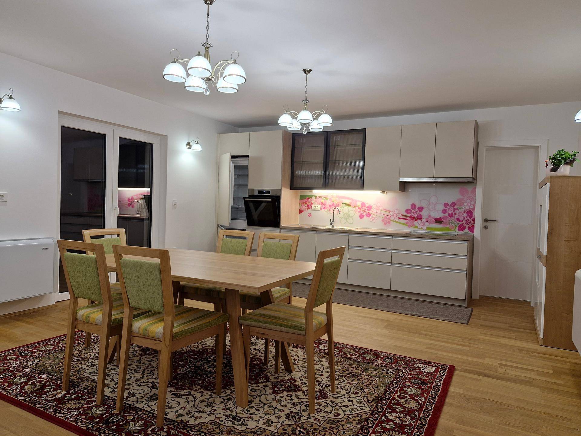 Heller Wohn-Essbereich mit Holzboden, Esstisch und moderner Küche mit floraler Rückwand.