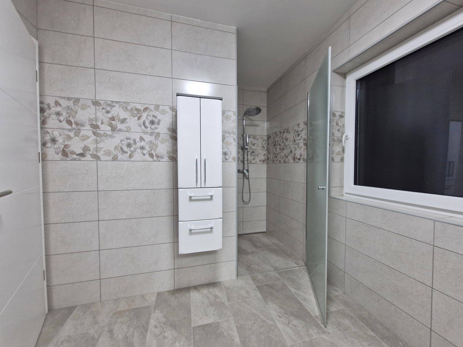 Helles Badezimmer mit begehbarer Dusche, Fenster und modernen Fliesen an Wänden und Boden.