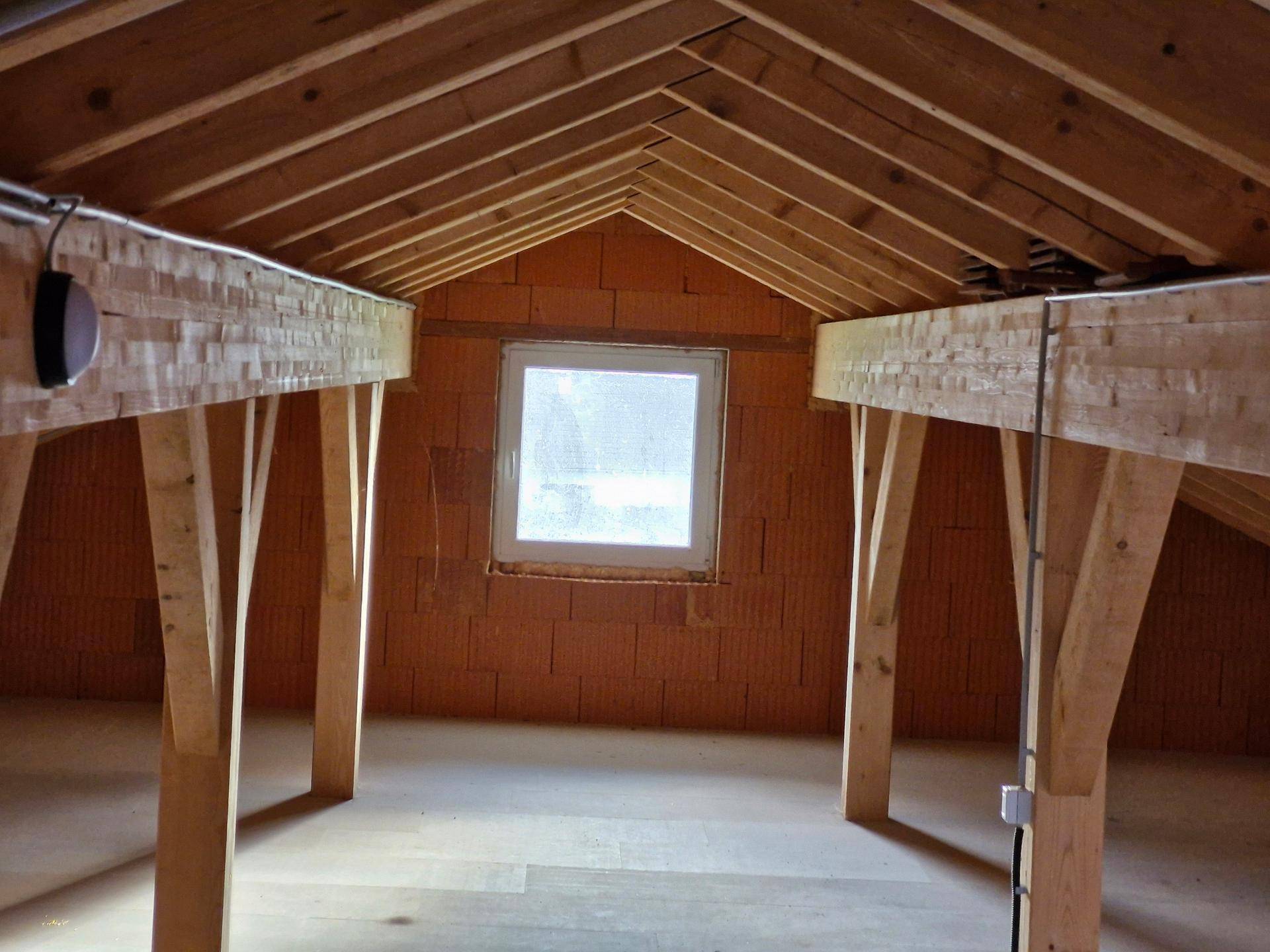 Unausgebauter Dachboden mit sichtbaren Holzbalken und Fenster, bietet Ausbaupotenzial.