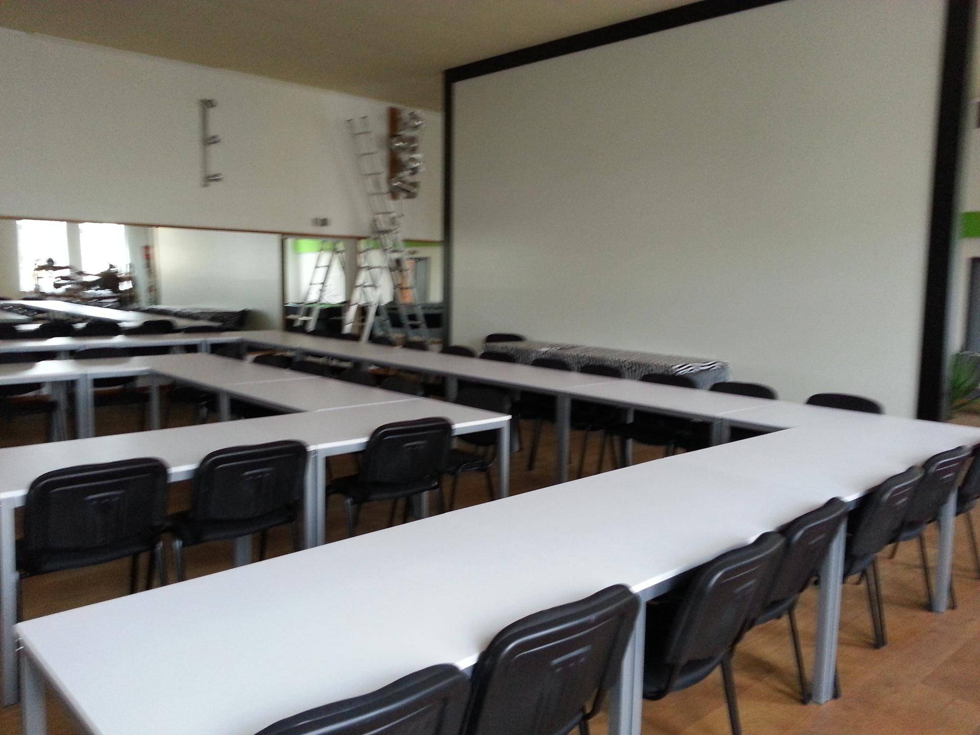 Konferenzraum mit U-förmiger Tischordnung und Stühlen, großer Projektionsfläche und Spiegelwand.