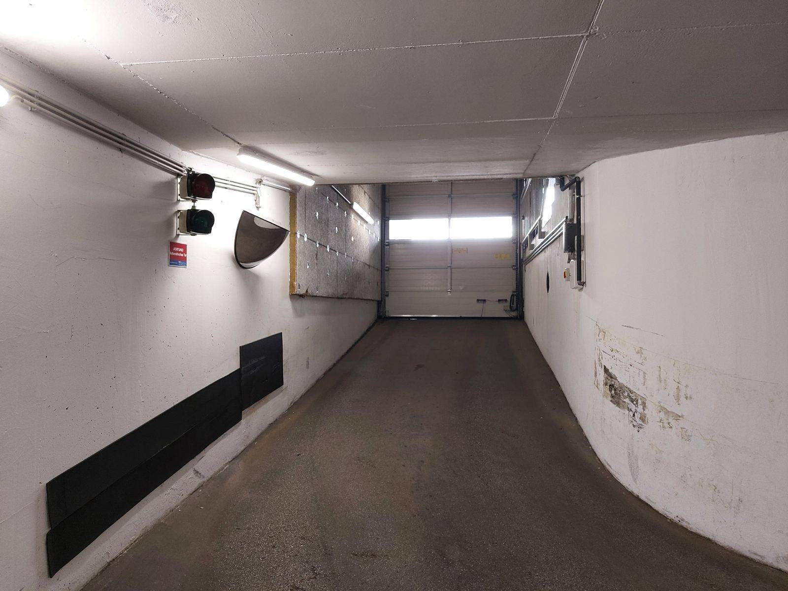 Einfahrt zur Tiefgarage mit Rampe, Beleuchtung und Verkehrsampel.