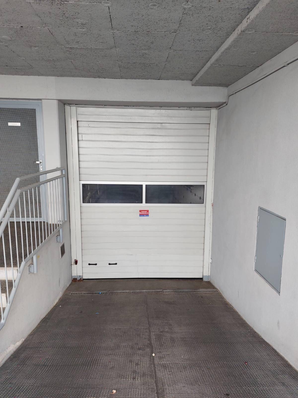 Nahaufnahme des Rolltors zur Tiefgarage mit Rampe und Handlauf.