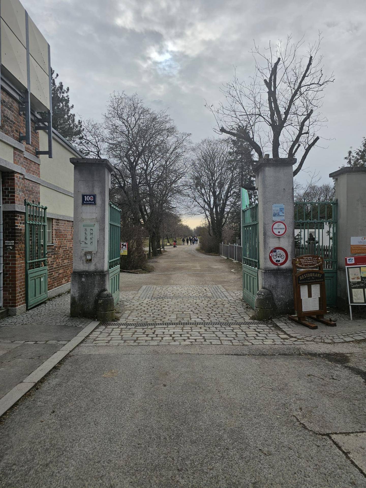 Eingang zu einem Park oder einer Grünanlage mit breitem Weg und Bäumen.