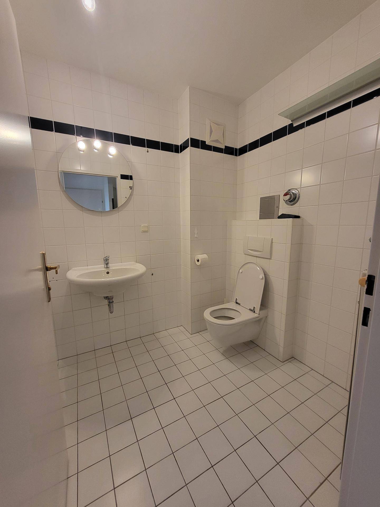 Gefliestes Badezimmer mit WC, Waschbecken und einem runden Spiegel, in gutem Zustand.