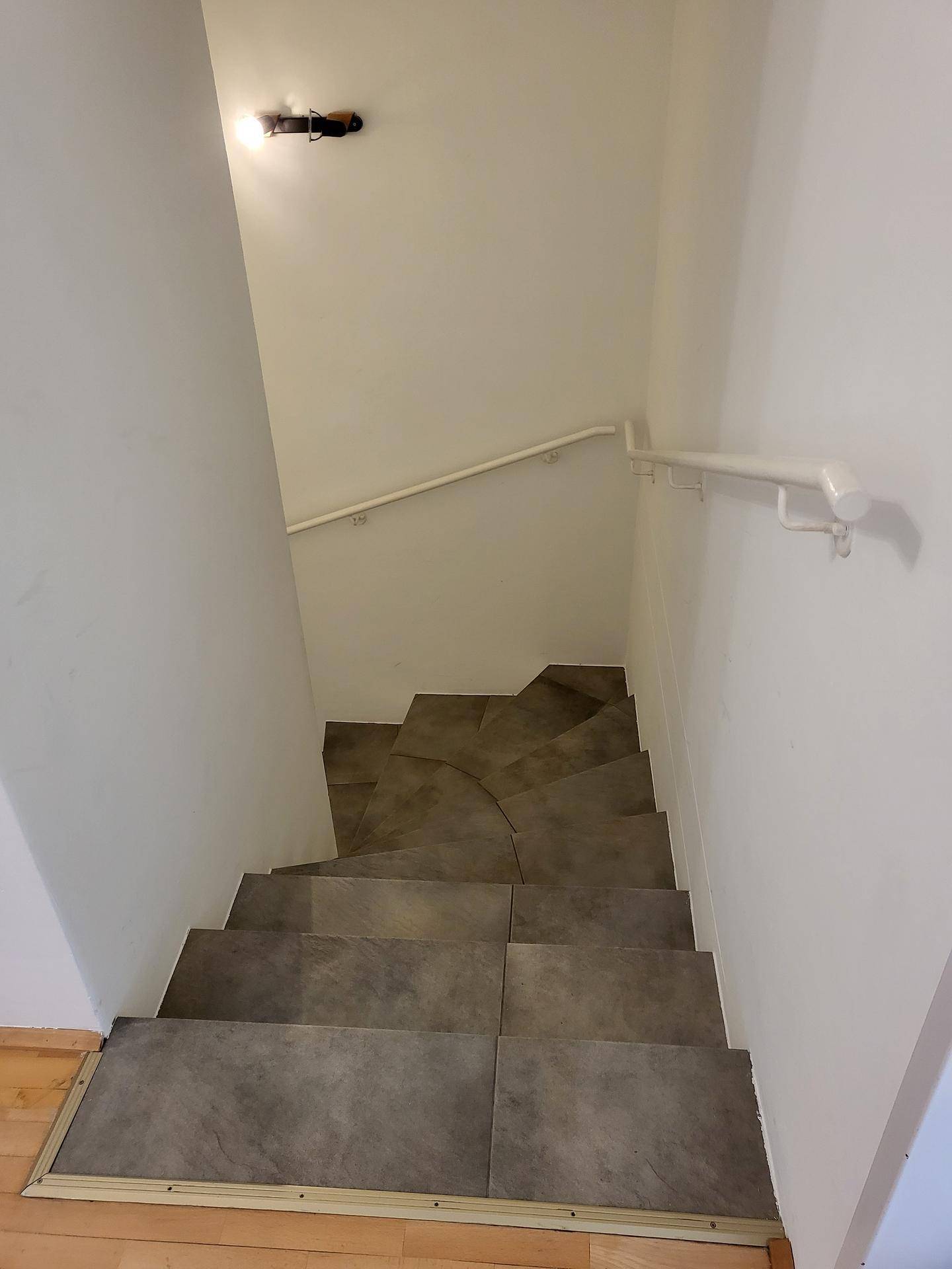 Treppenhaus mit gefliesten Stufen und Handlauf, das zu den unteren Etagen führt.