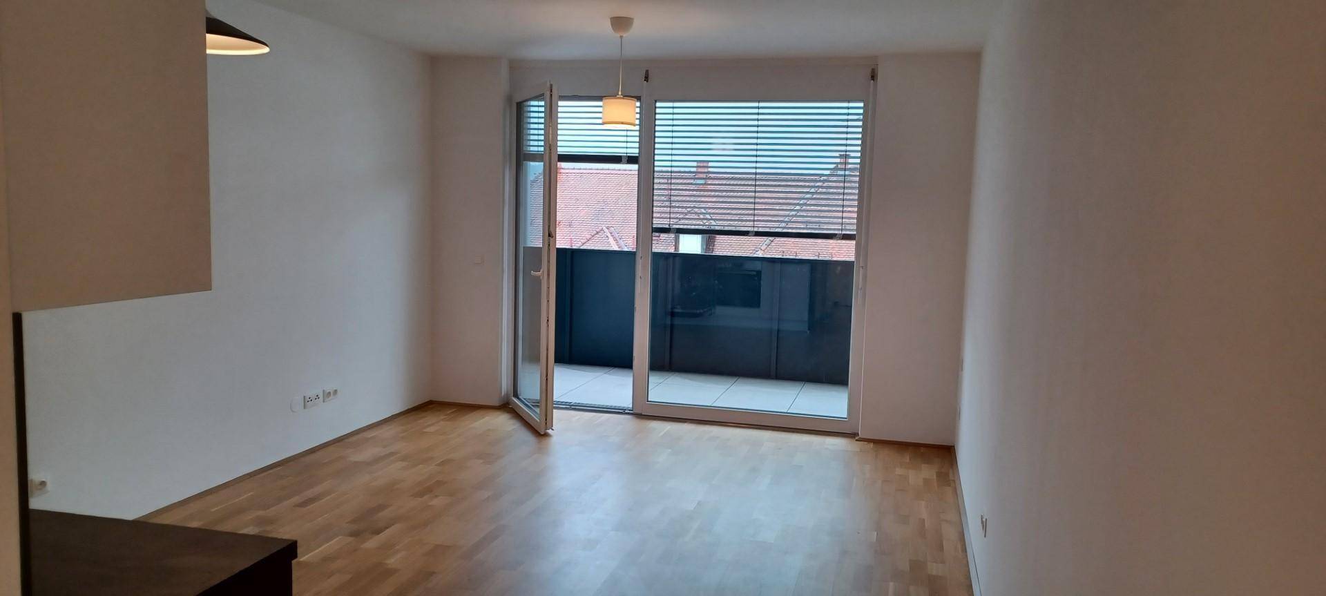 Heller Wohnraum mit Holzboden und großer Balkontür, die viel Tageslicht hereinlässt.