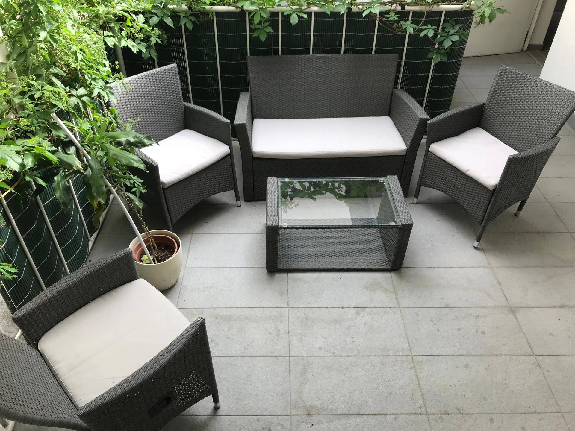 Geräumige Terrasse mit bequemen Rattanmöbeln und einem Glastisch, umgeben von Pflanzen.