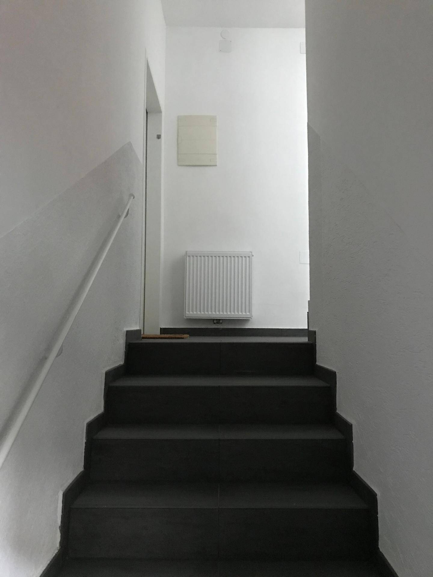 Treppenhaus mit dunklen Stufen und weißem Geländer, das in die obere Etage führt.