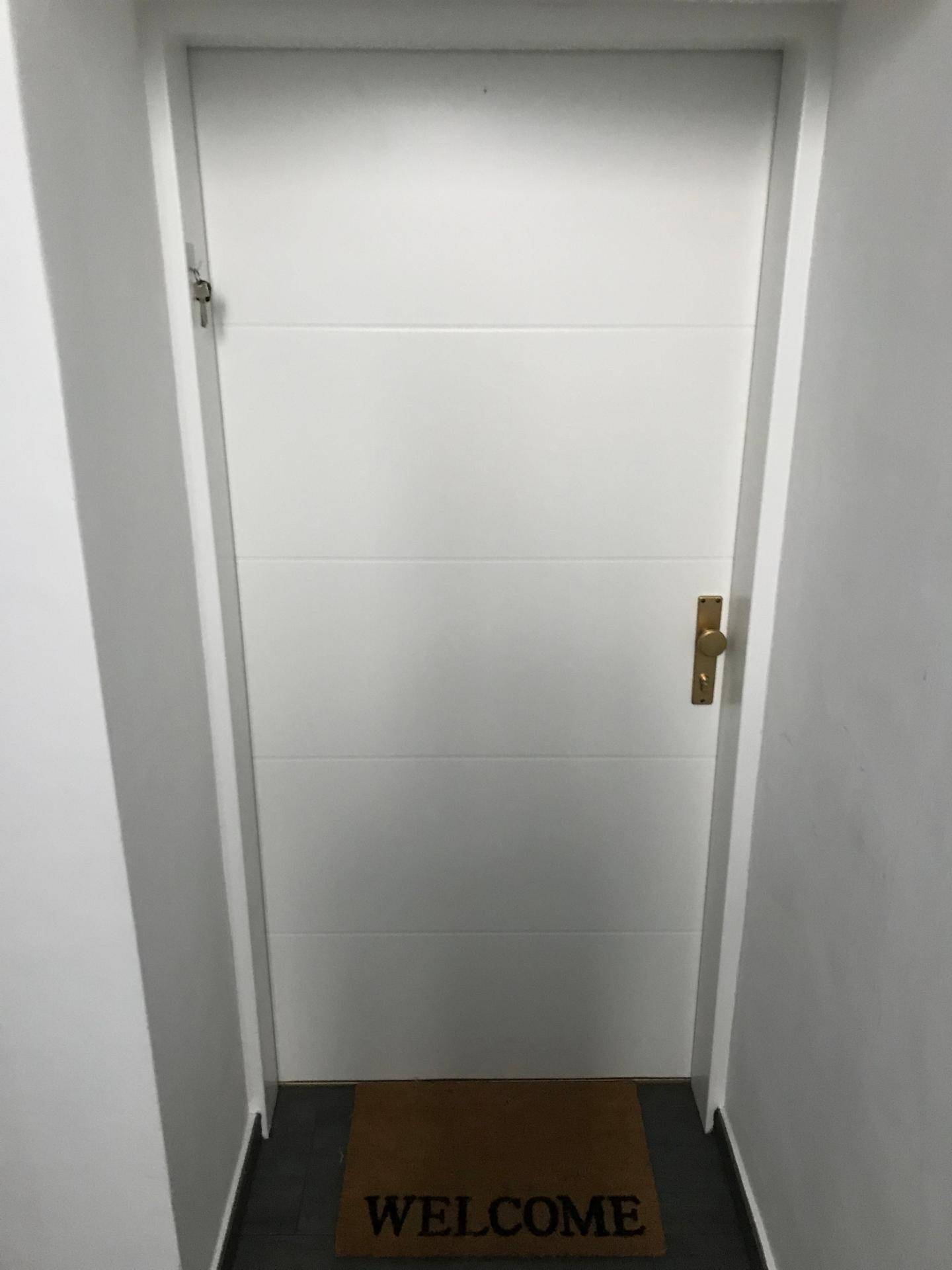 Eingangstür mit Willkommensmatte und schlichtem Design in einem hellen, einladenden Flur.
