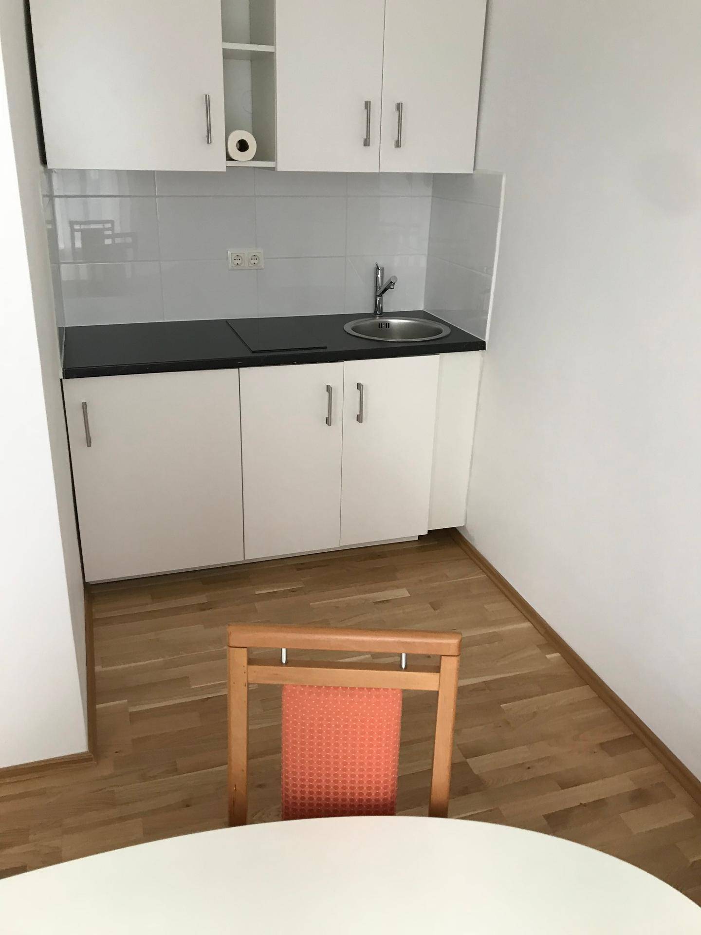 Kleine Küchenzeile mit weißen Schränken, Spüle und Kochfeld, ideal für kompaktes Wohnen.