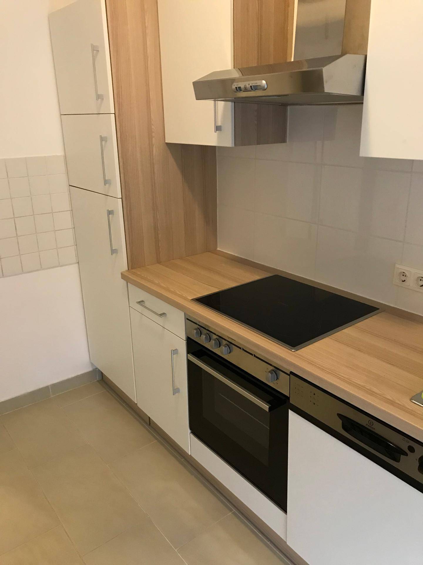 Moderne Einbauküche mit hellen Holzfronten, Induktionskochfeld, Backofen und Dunstabzugshaube.