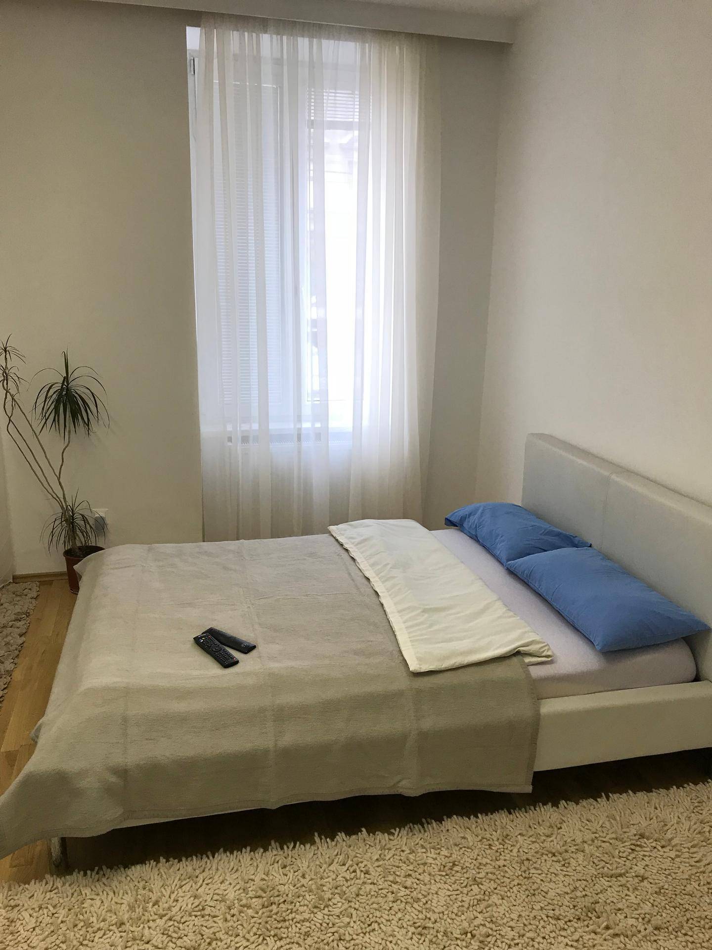 Helles Schlafzimmer mit Doppelbett, Teppichboden und großem Fenster, das viel Tageslicht hereinlässt.