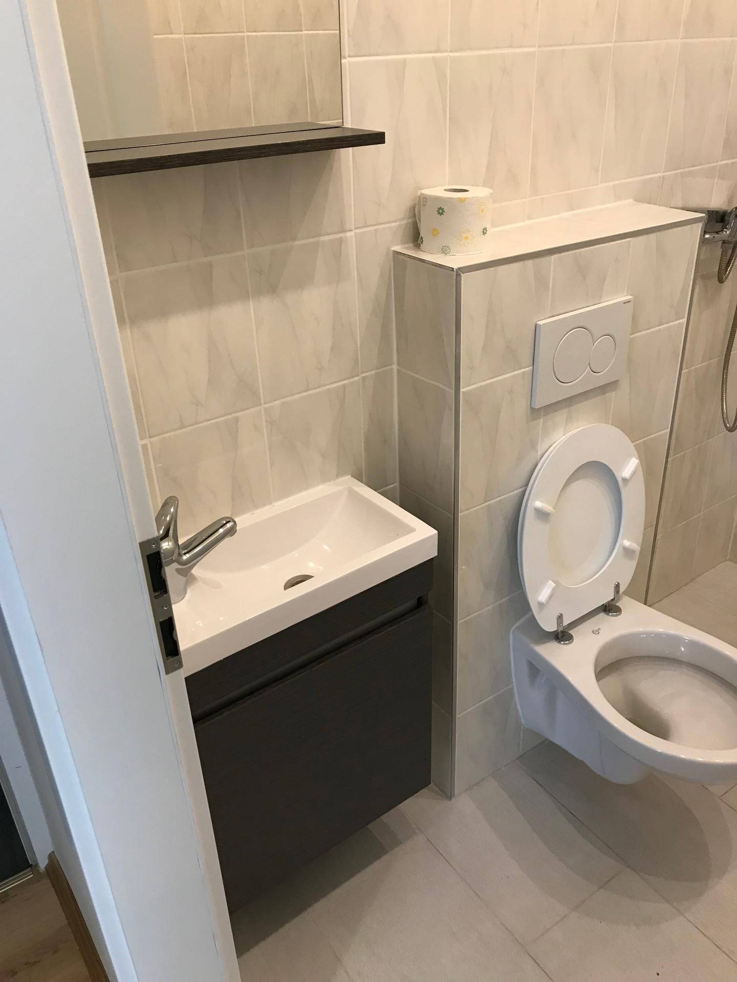 Modernes WC mit wandhängender Toilette und kleinem Waschbecken in hellen Fliesen.