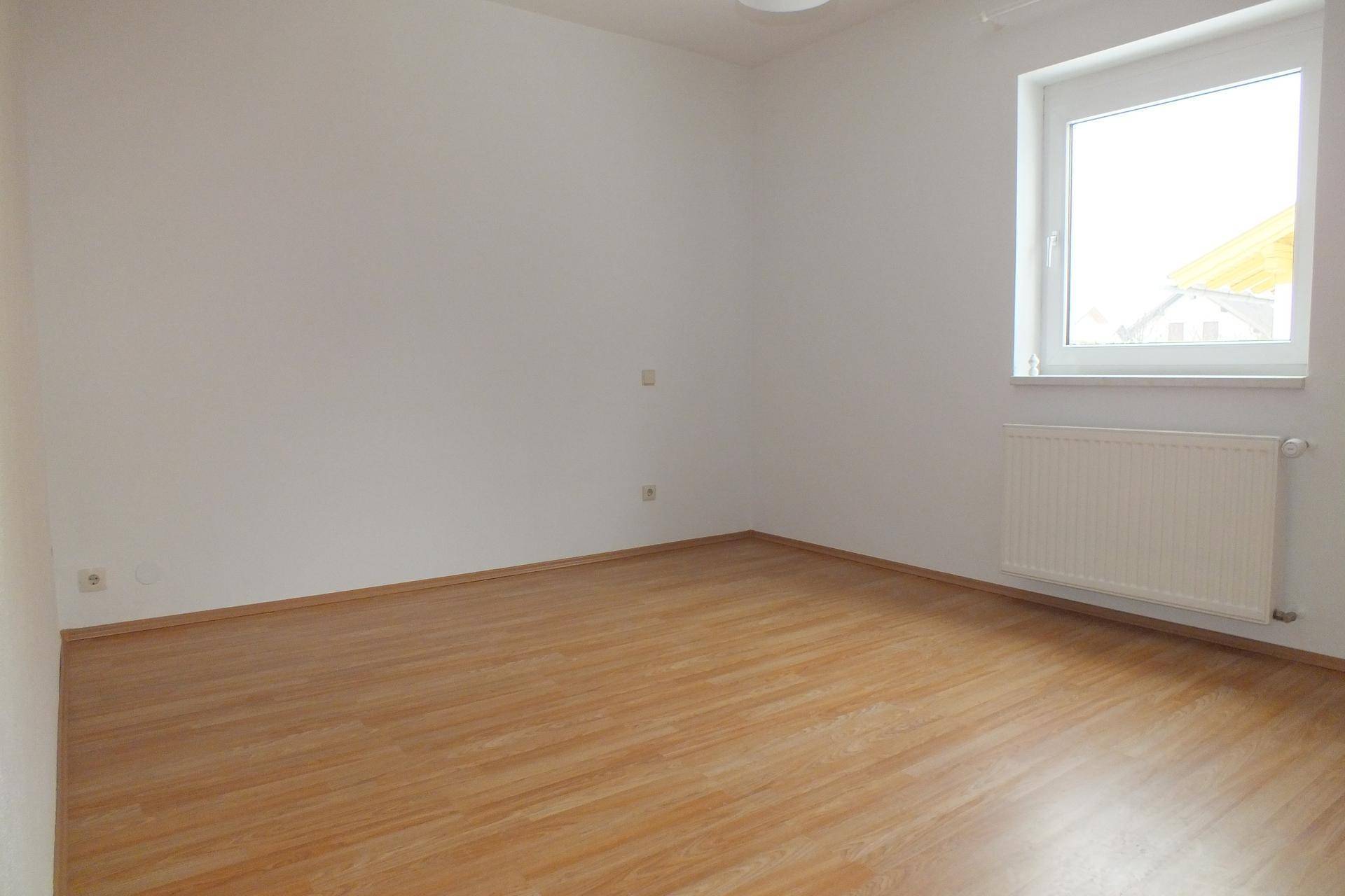 Helles Schlafzimmer mit Laminatboden, weiß gestrichenen Wänden und großem Fenster.