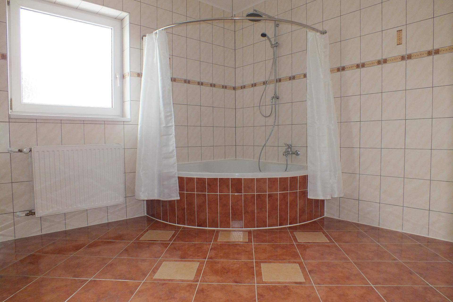 Badezimmer mit Eckbadewanne, Duschvorhang und braunen Fliesen.